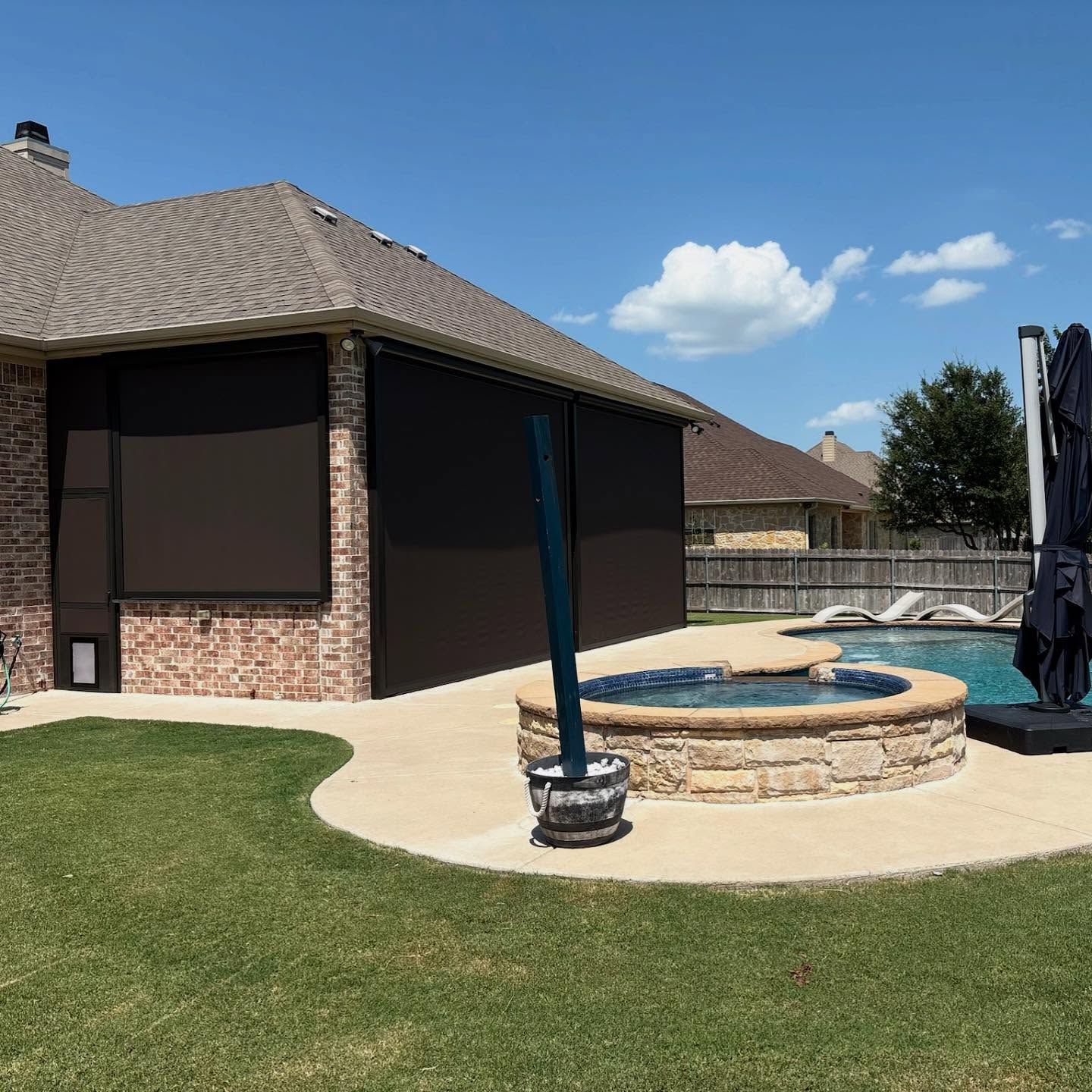 Backyard with a pool, hot tub, and patio. A house has retractable black screens.