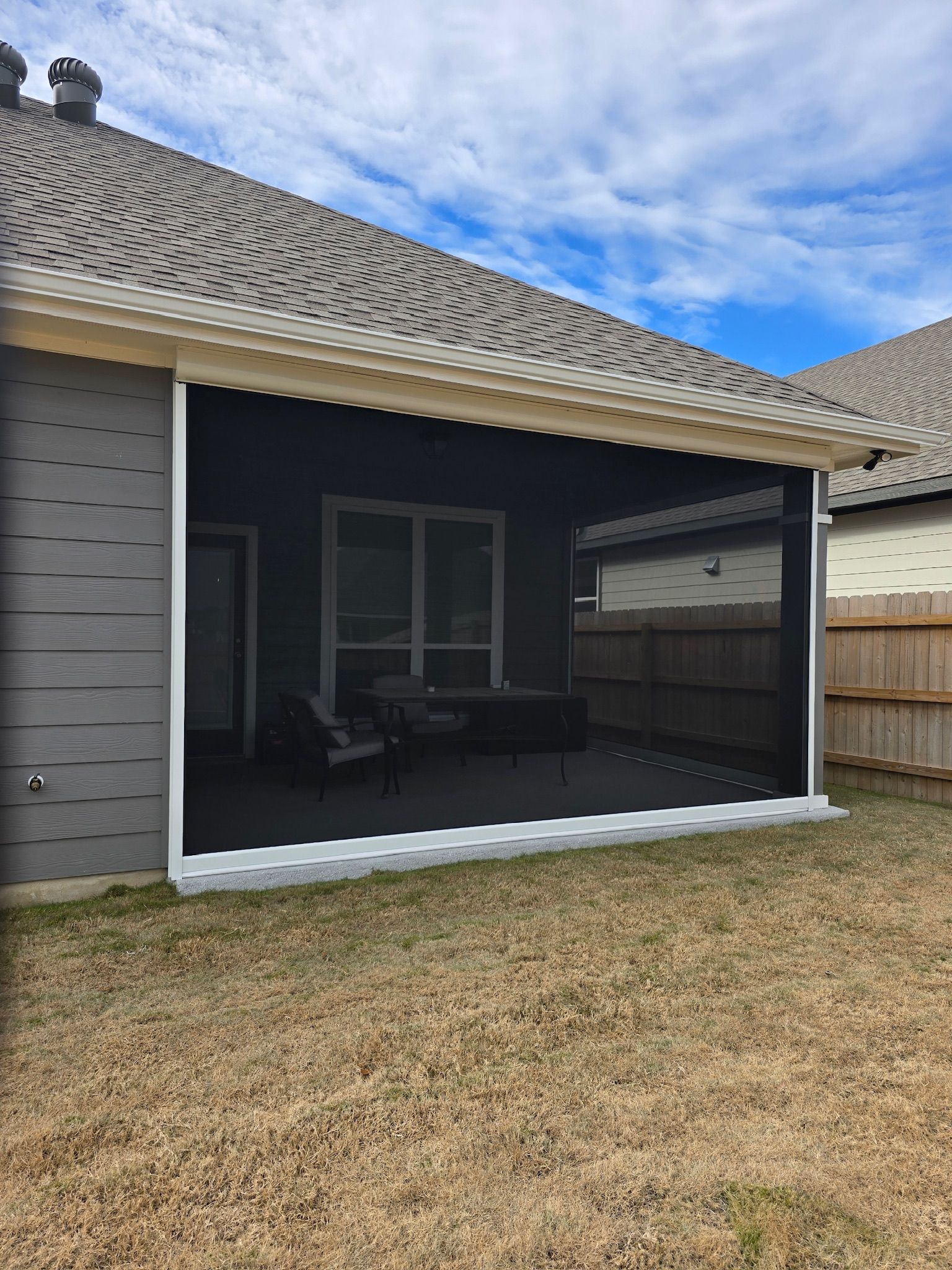 Outdoor patio enclosed with black screens, gray siding, and a brown roof against a blue sky.