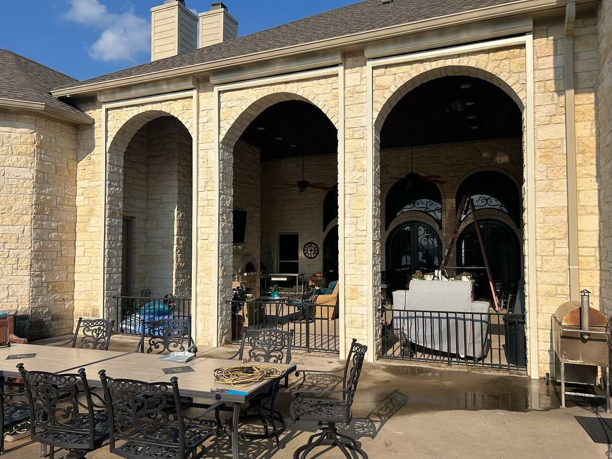 Stone patio with arched openings, wrought iron furniture, and a grill.