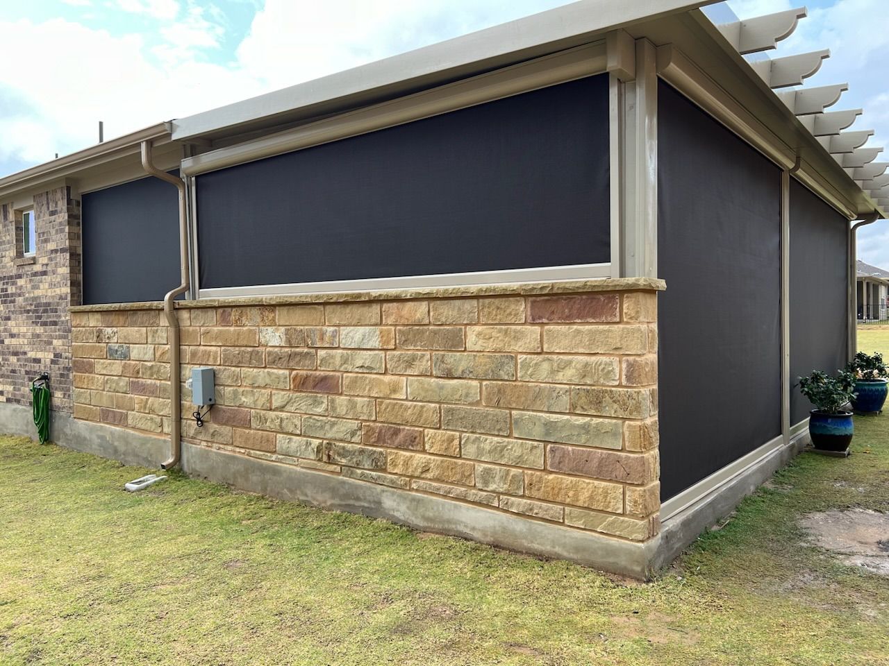 Outdoor patio with black shades, brick wall, and pergola.
