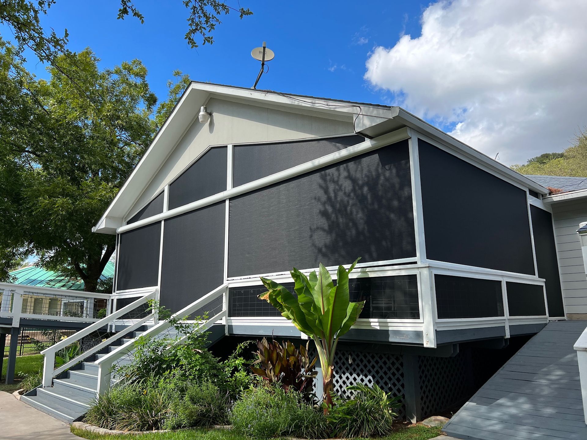 House with screened porch, dark screens, white trim, gray stairs, and surrounding greenery.