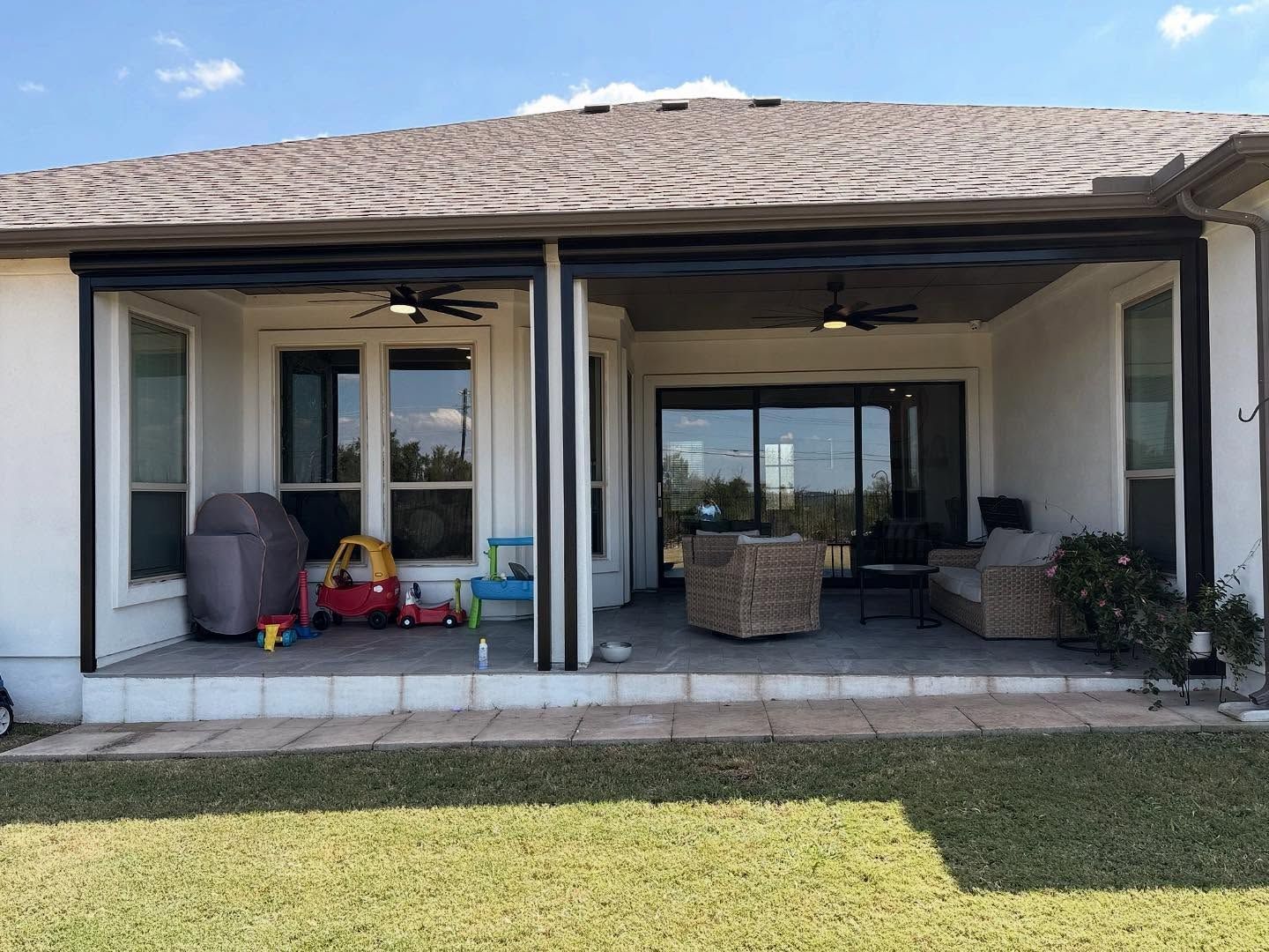 Covered patio with retractable screens, fans, and furniture. Lawn in foreground, house in background.