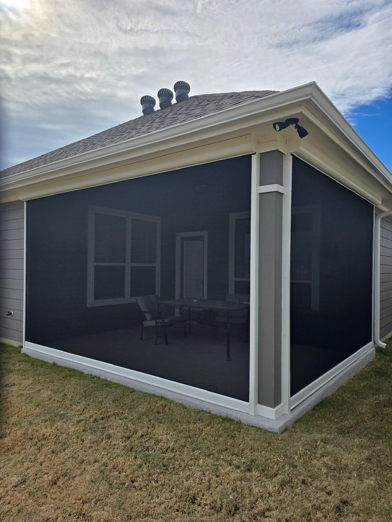 Screened-in porch with dark mesh and white trim.  Inside, patio furniture is visible.  Overcast sky.