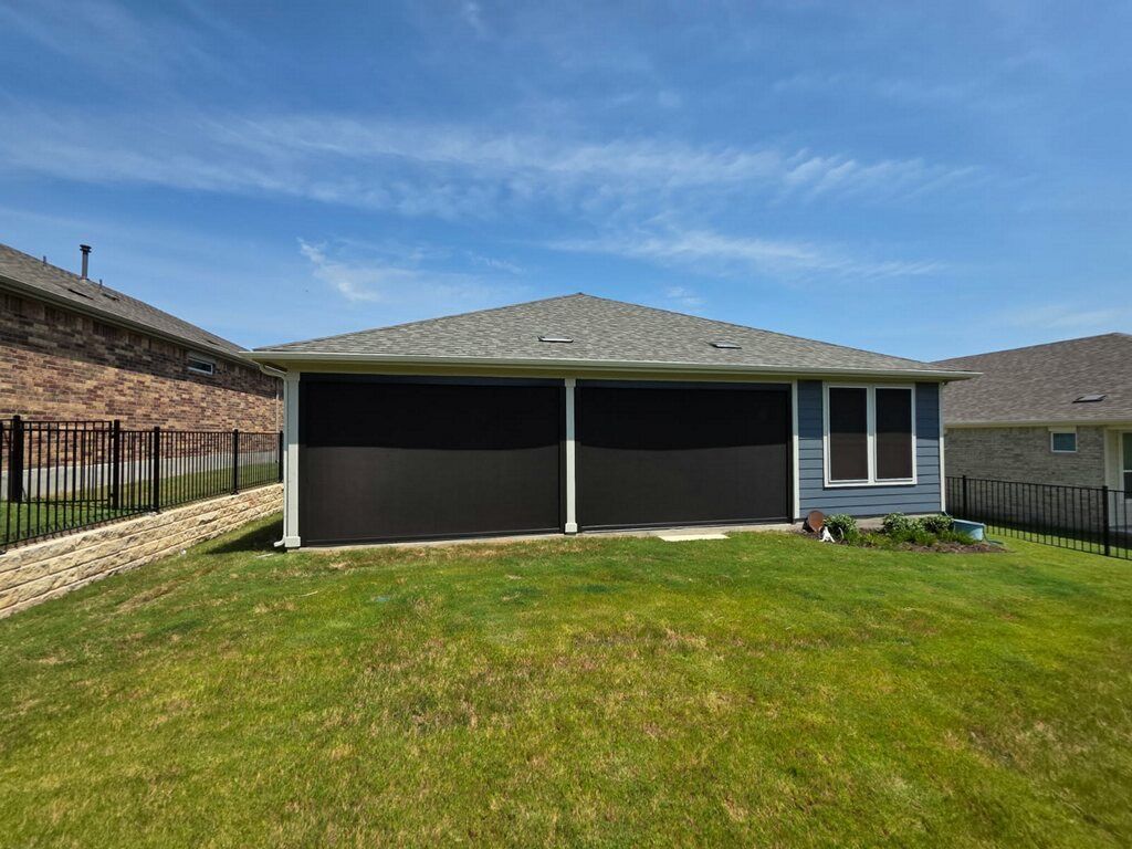 Back of a house with two large screened openings and a window, against a blue sky. Green grass in the foreground.