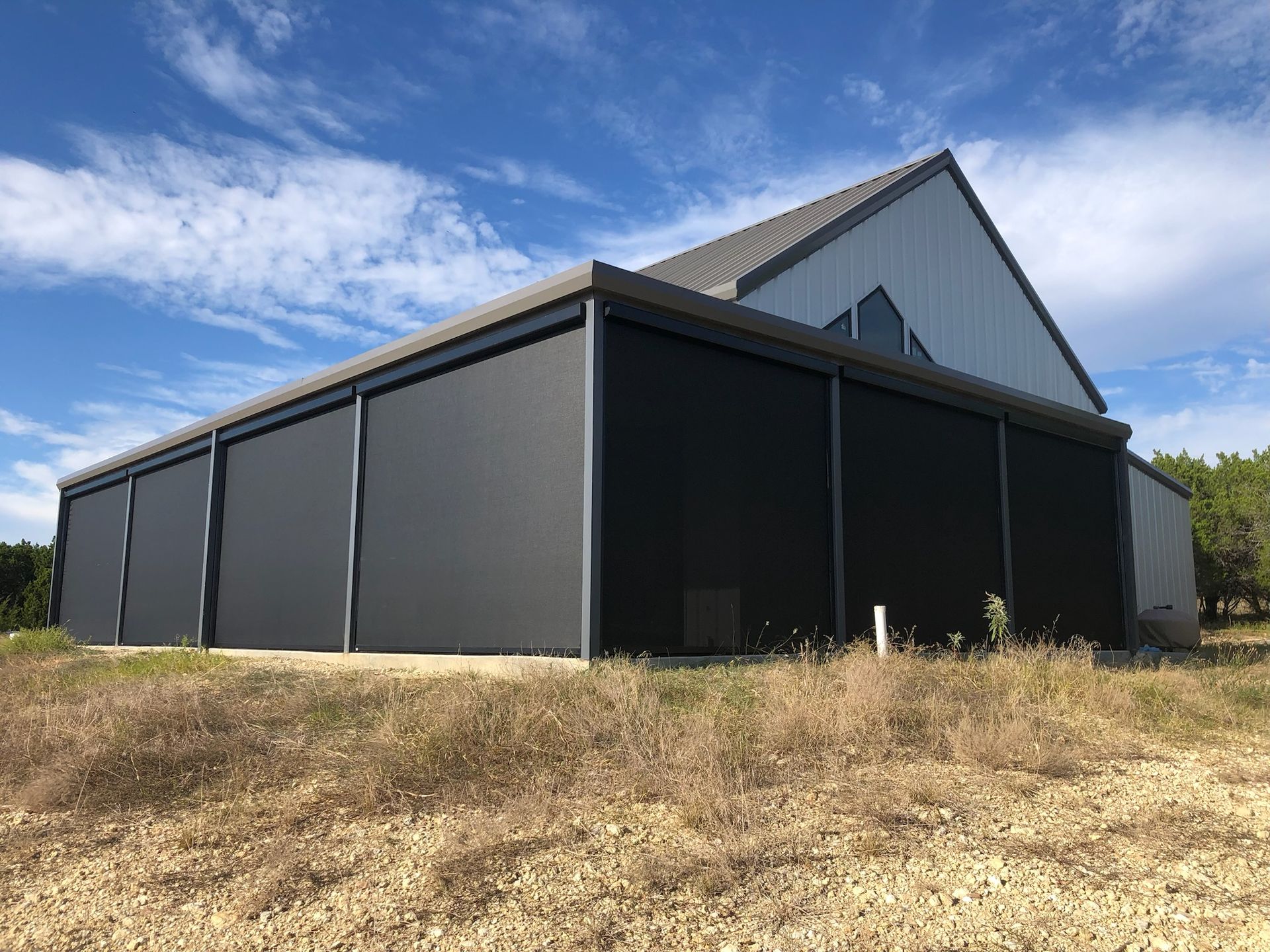 Dark gray building with a sloped roof. The building has large, dark gray panels and is set in a field with blue sky.