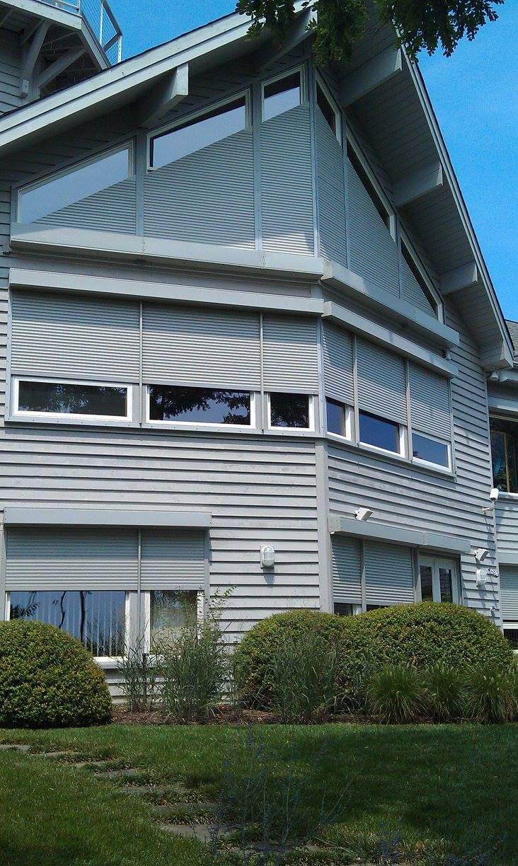 Gray building with multiple windows, awnings, and shrubs.