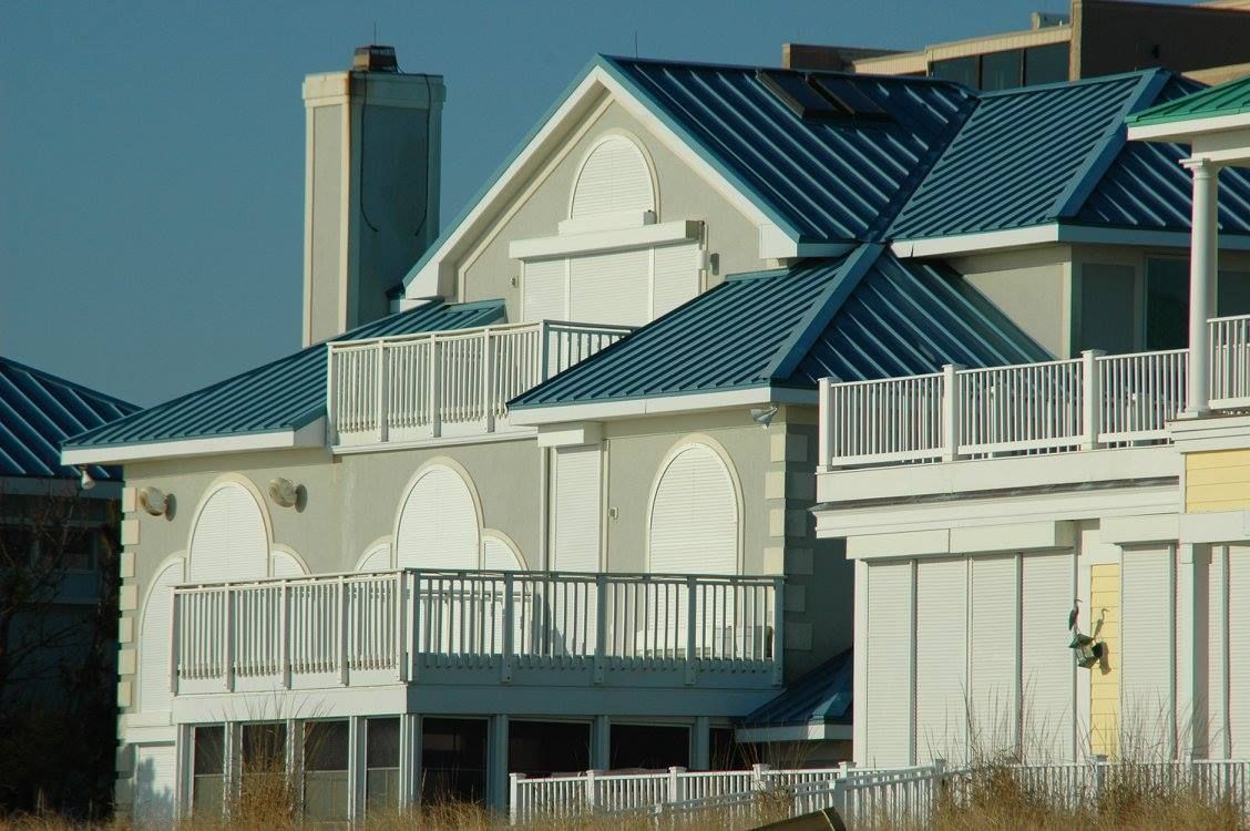 Blue-roofed, multi-story beach houses with white balconies and shutters on a sunny day.