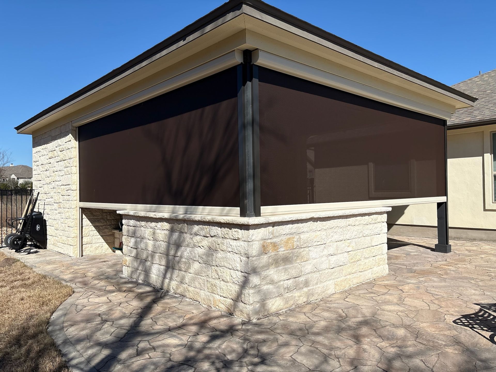 Outdoor bar area with a brown sun shade; stone wall and patio.