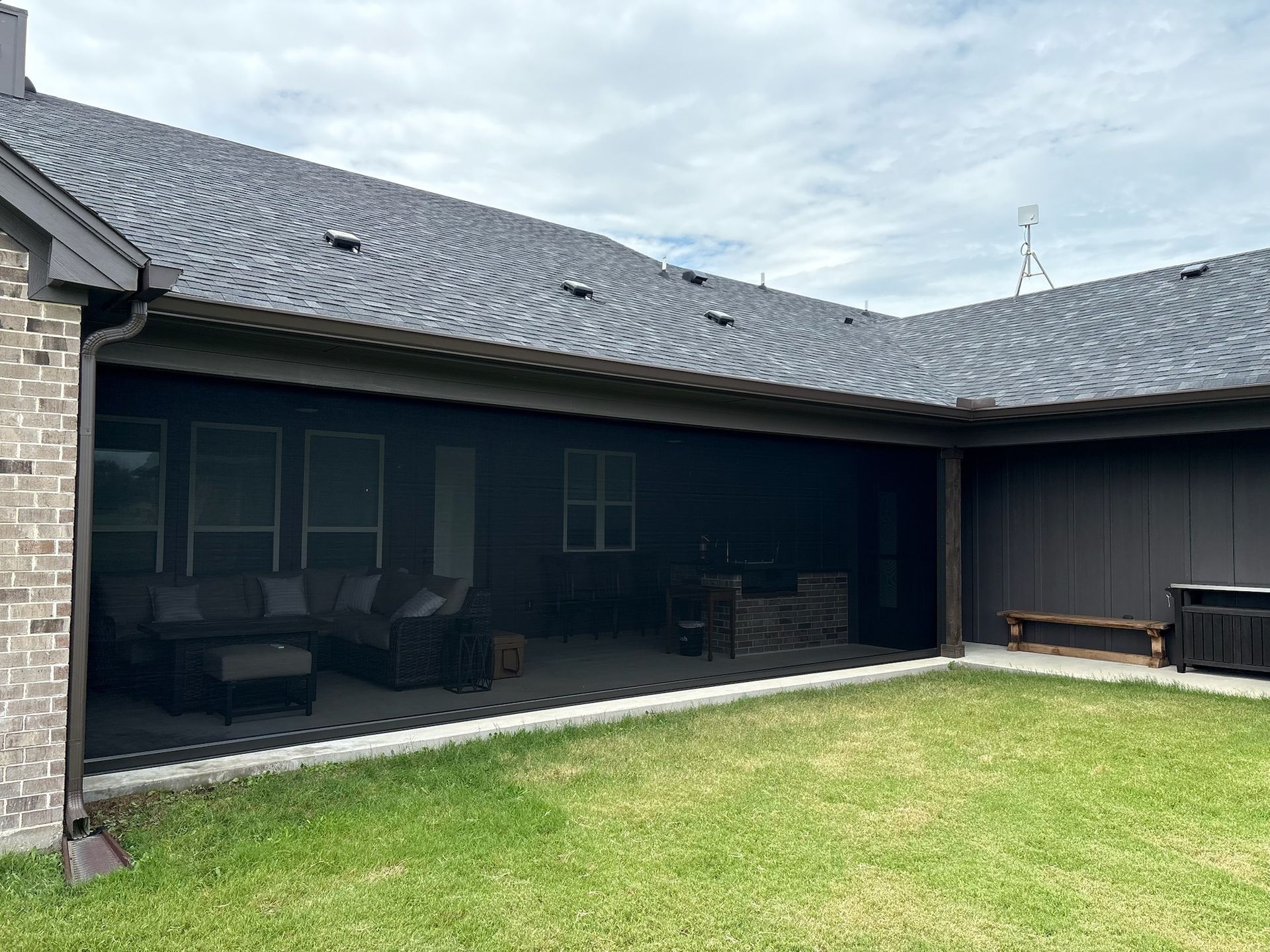 Screened-in patio attached to a house with dark roof and trim. Green grass and overcast sky.