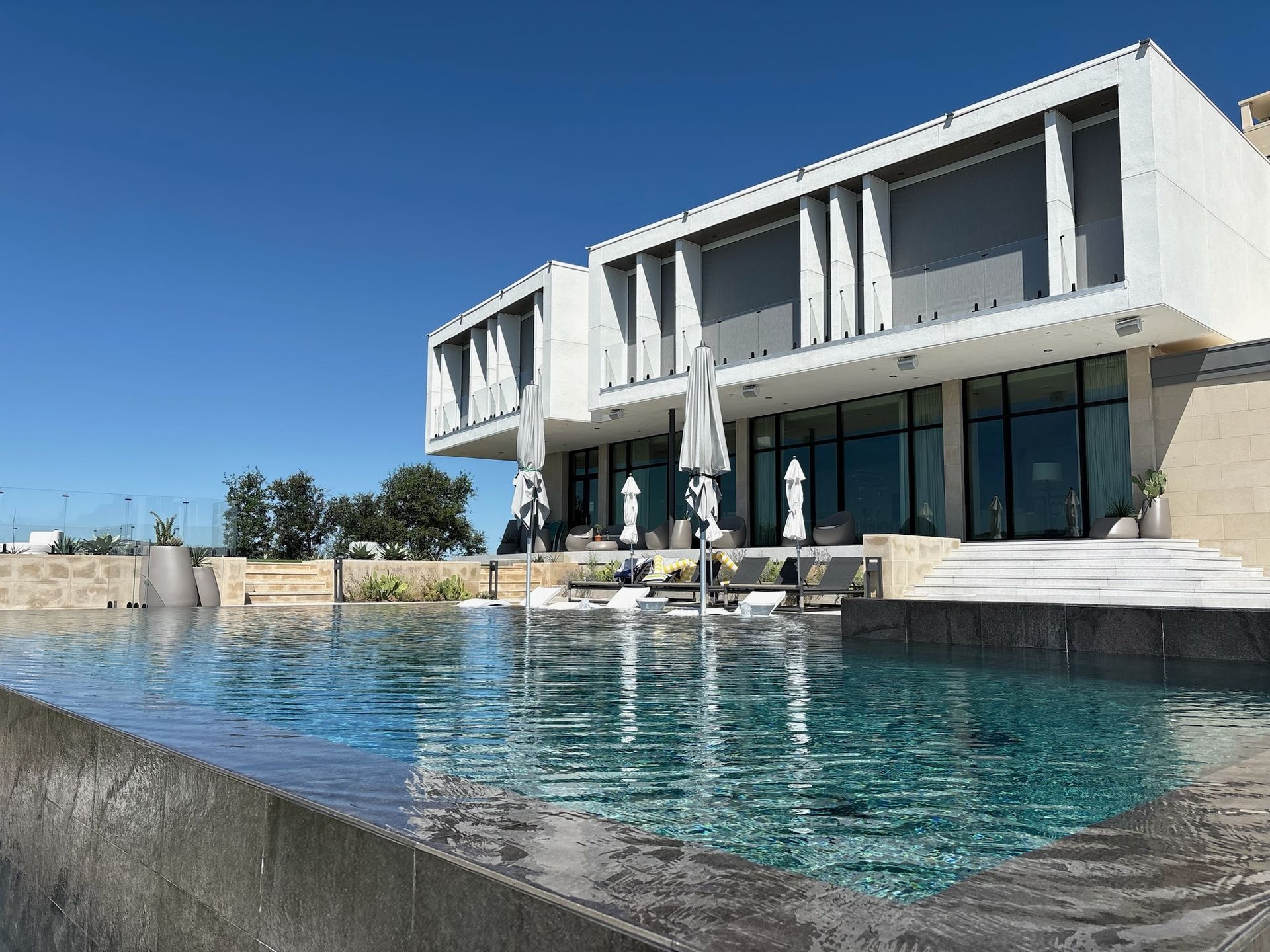 Modern white building with large windows and infinity pool on a sunny day.