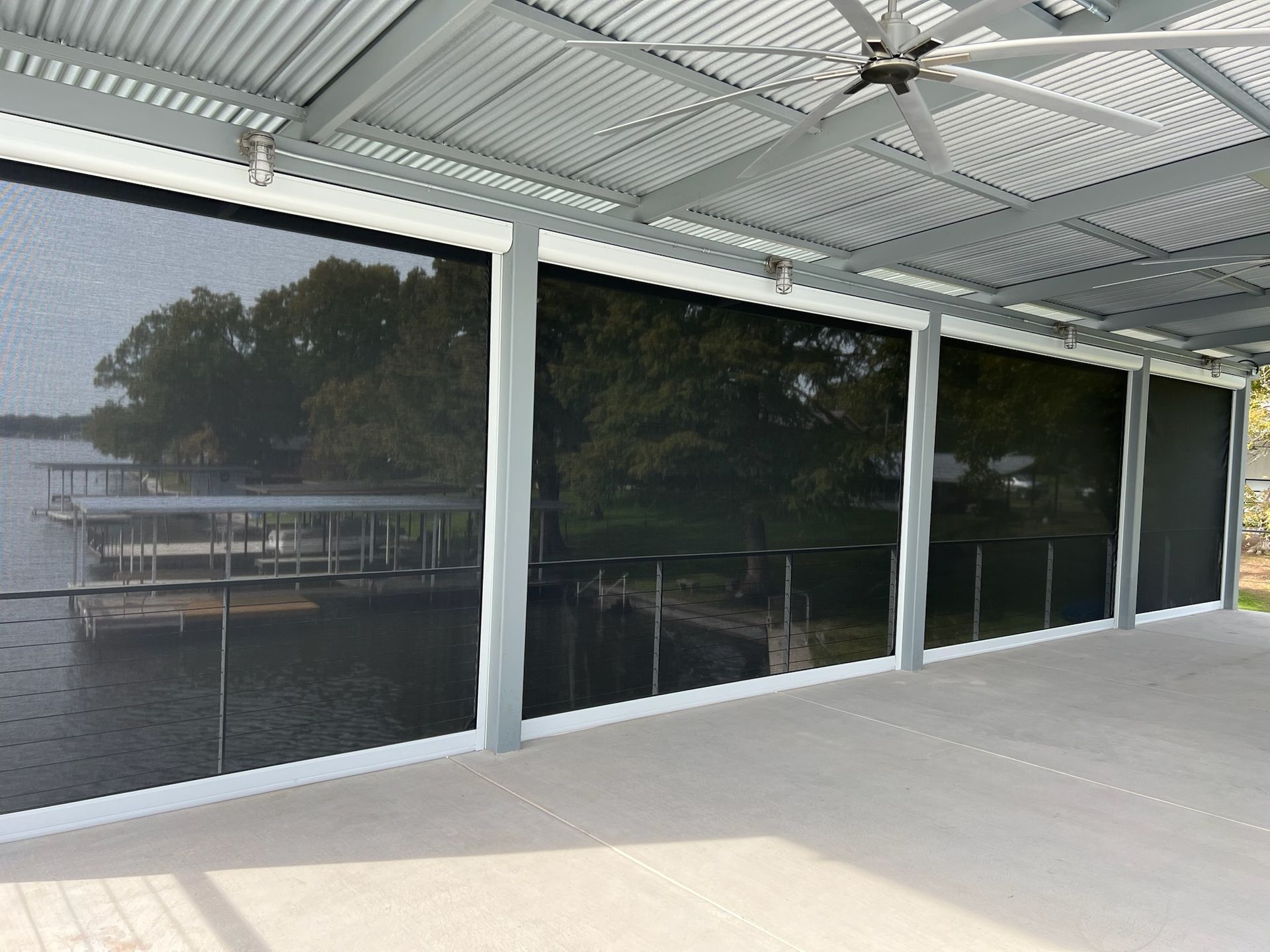 Patio with retractable black sunscreens, overlooking a lake with a dock.