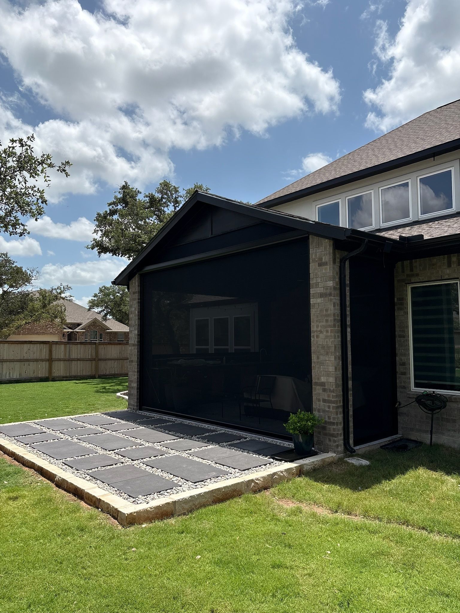 Black screened porch with stone facade, under a house, with a cloudy sky overhead.