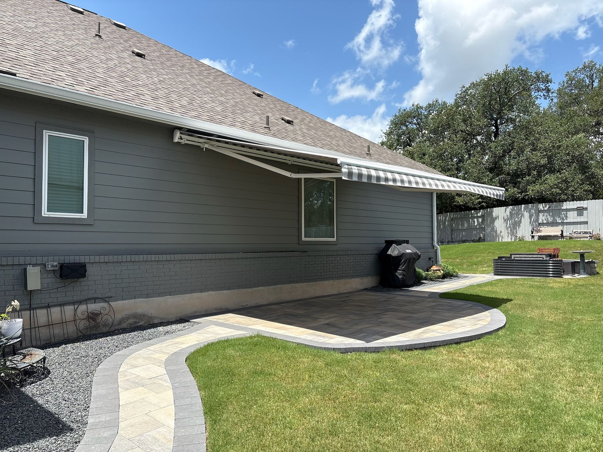 Exterior view of a gray house with an awning over a patio, stone path, and green lawn on a sunny day.