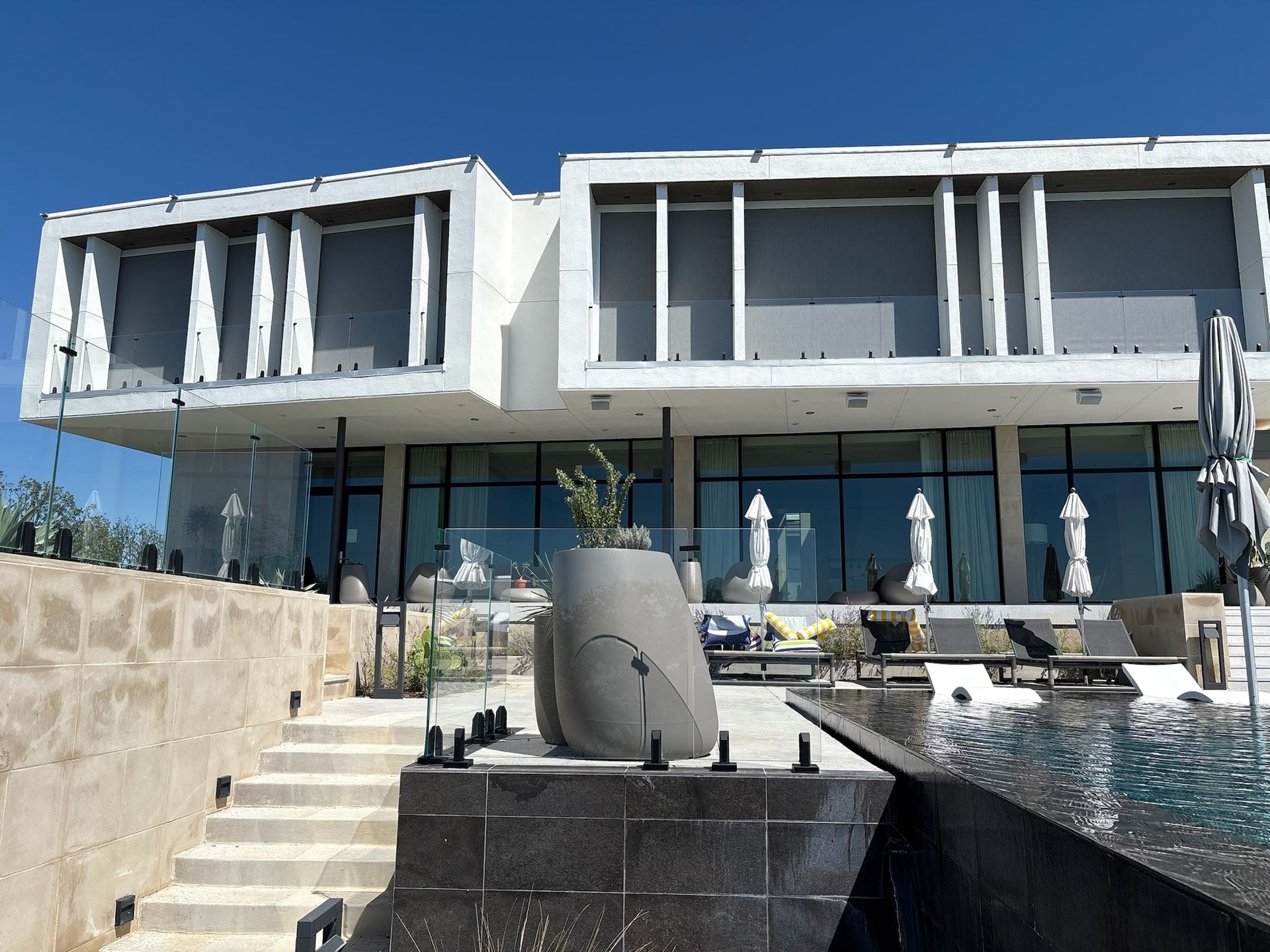 Modern, multi-story building with a pool, stairs, and large windows under a blue sky.