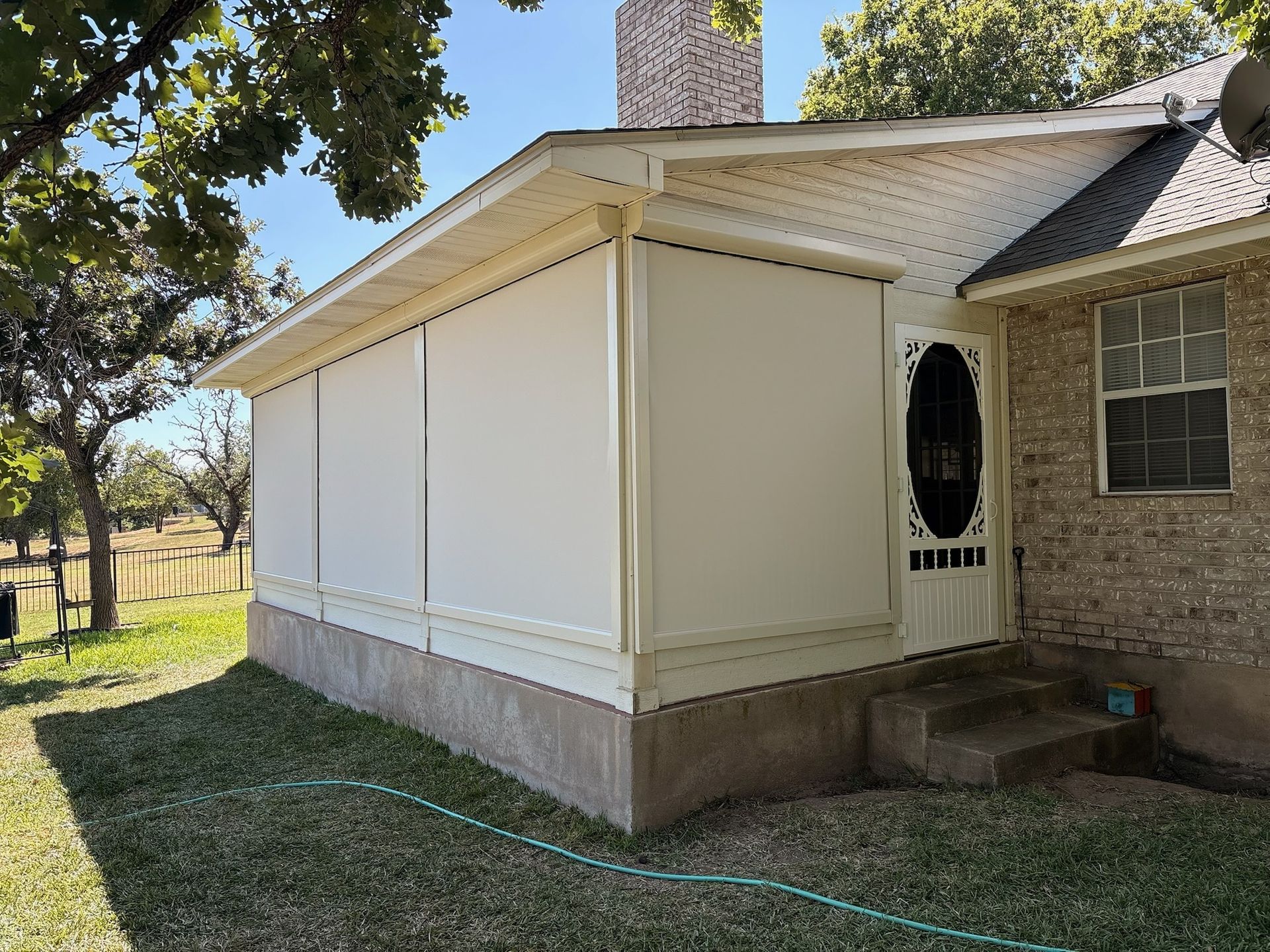 Enclosed porch with white retractable screens; beige siding, brick wall. Steps leading to a door.