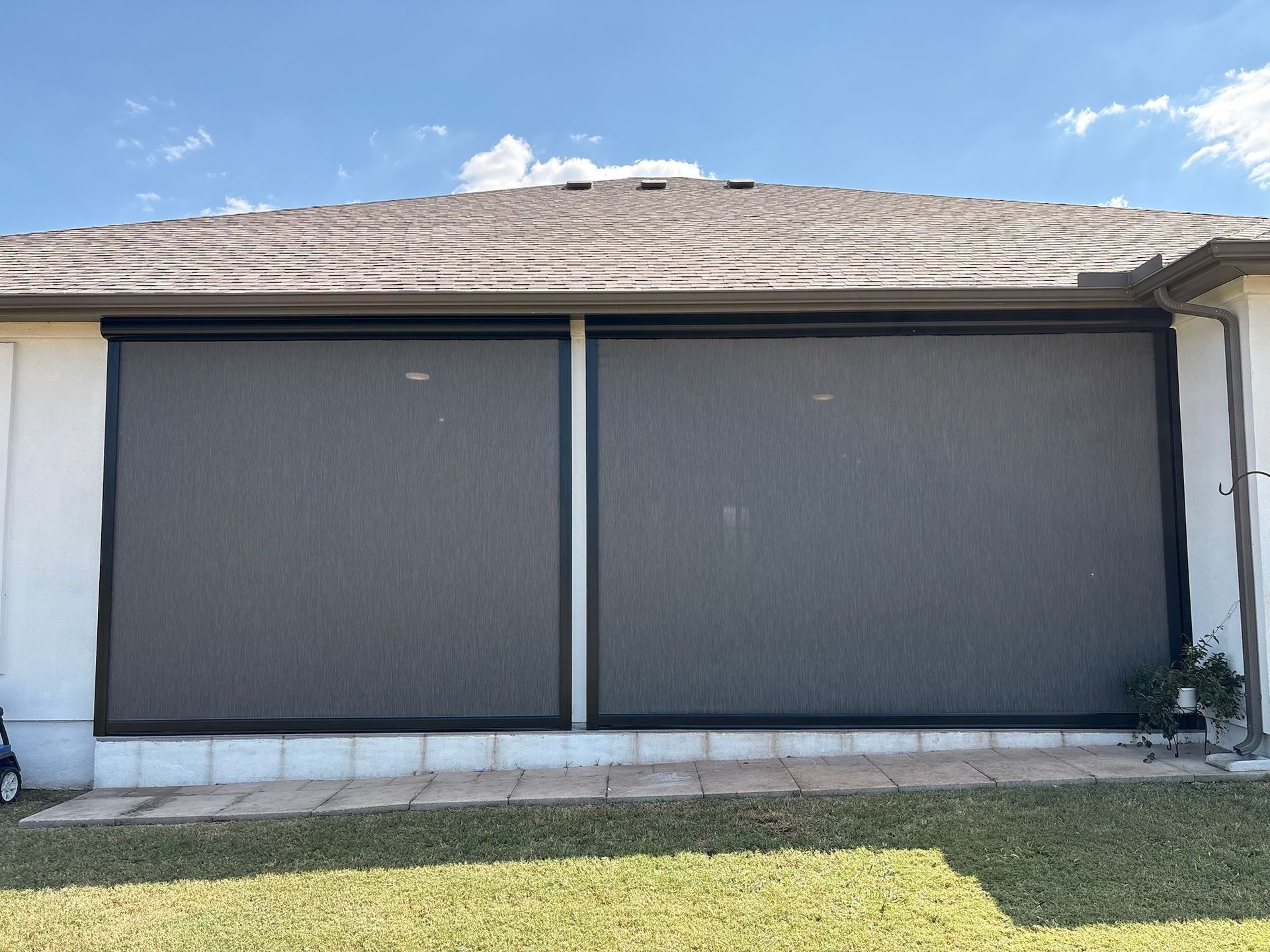Two large gray retractable screens on a white building exterior, under a brown roof, with a blue sky background.