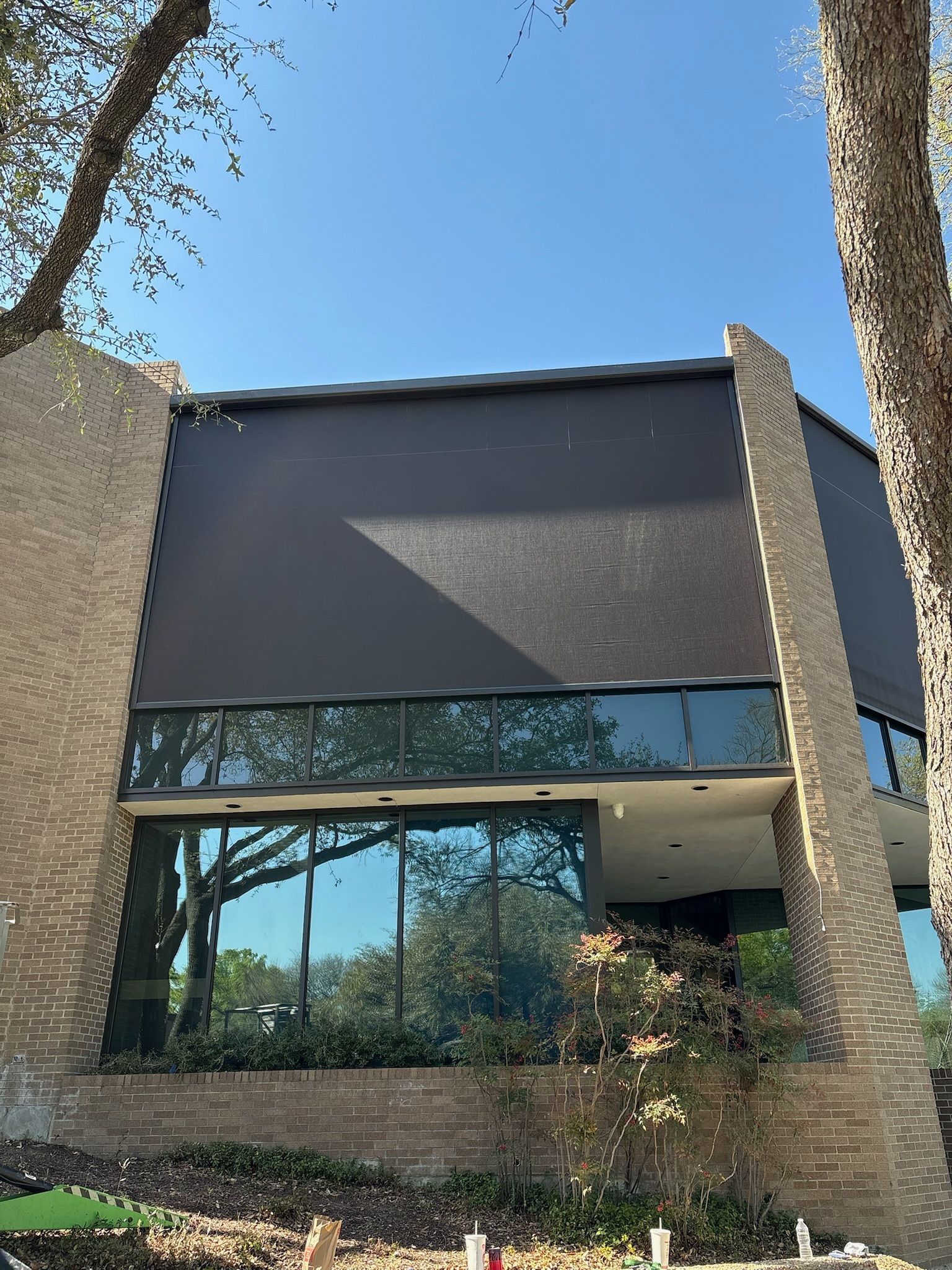 Building with dark textured facade, large windows, brick columns, trees, and blue sky.