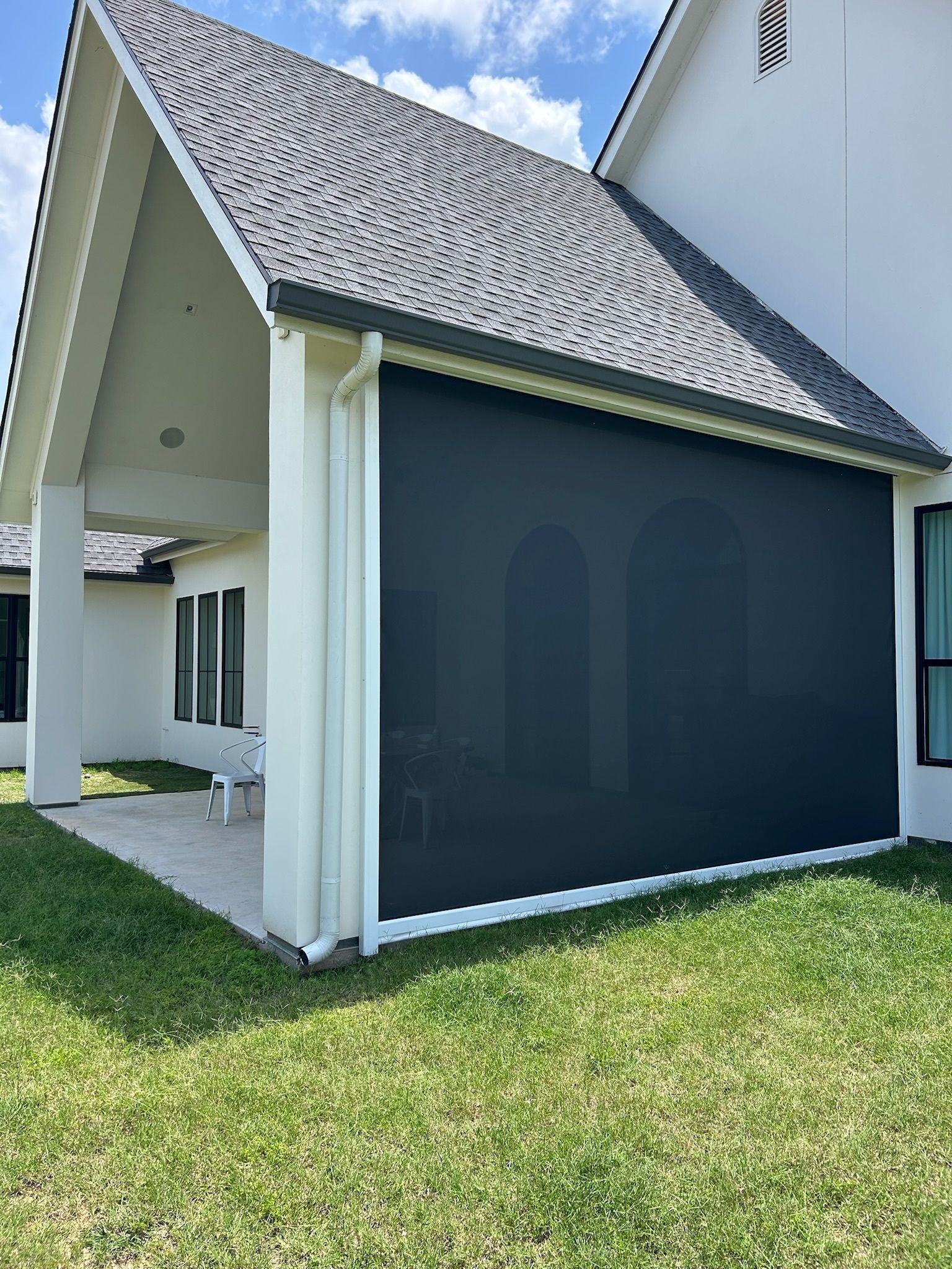 Black exterior shade on a house patio, white trim and roof, green grass and blue sky.