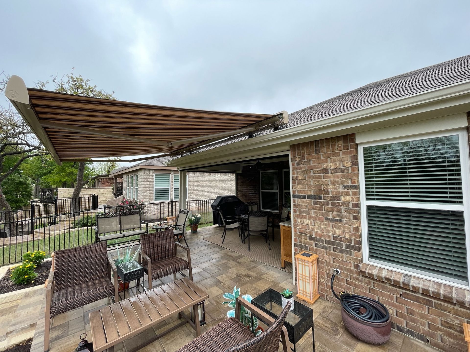 Backyard patio with retractable awning; brick house; brown and tan furniture; overcast sky.