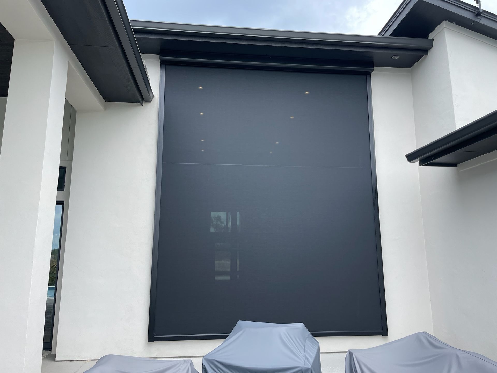 Dark gray outdoor shade covering large window on white building.