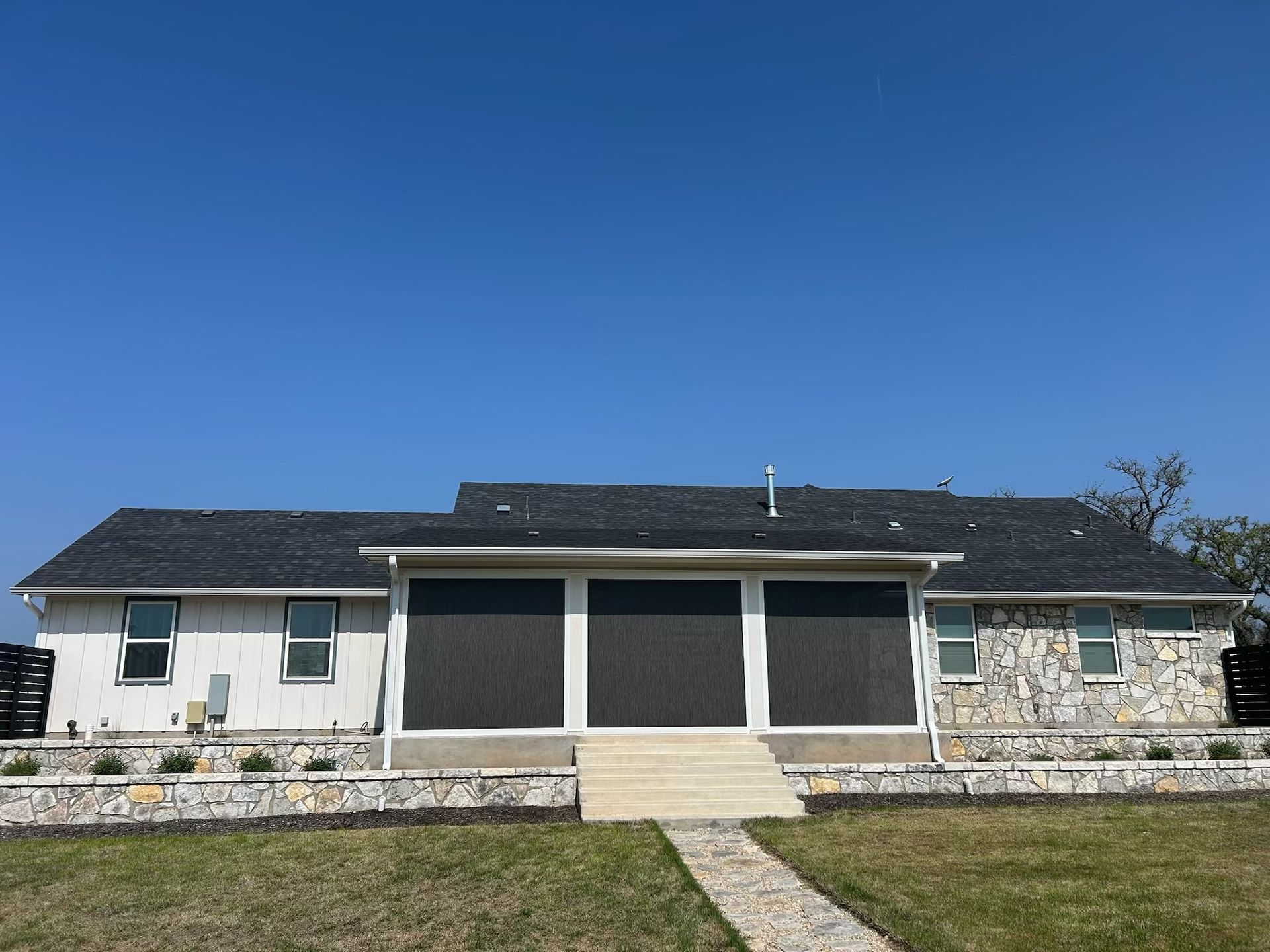 Back view of a house with a gray roof, white siding, and a screened-in porch, under a blue sky.