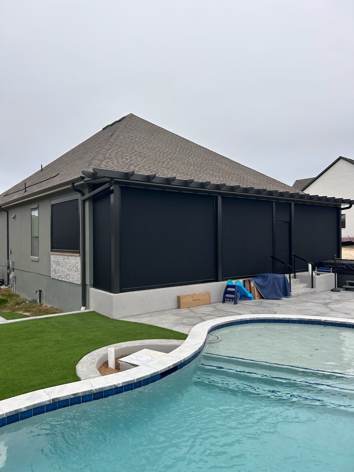 Outdoor living space with black retractable screens, pool, and green lawn.