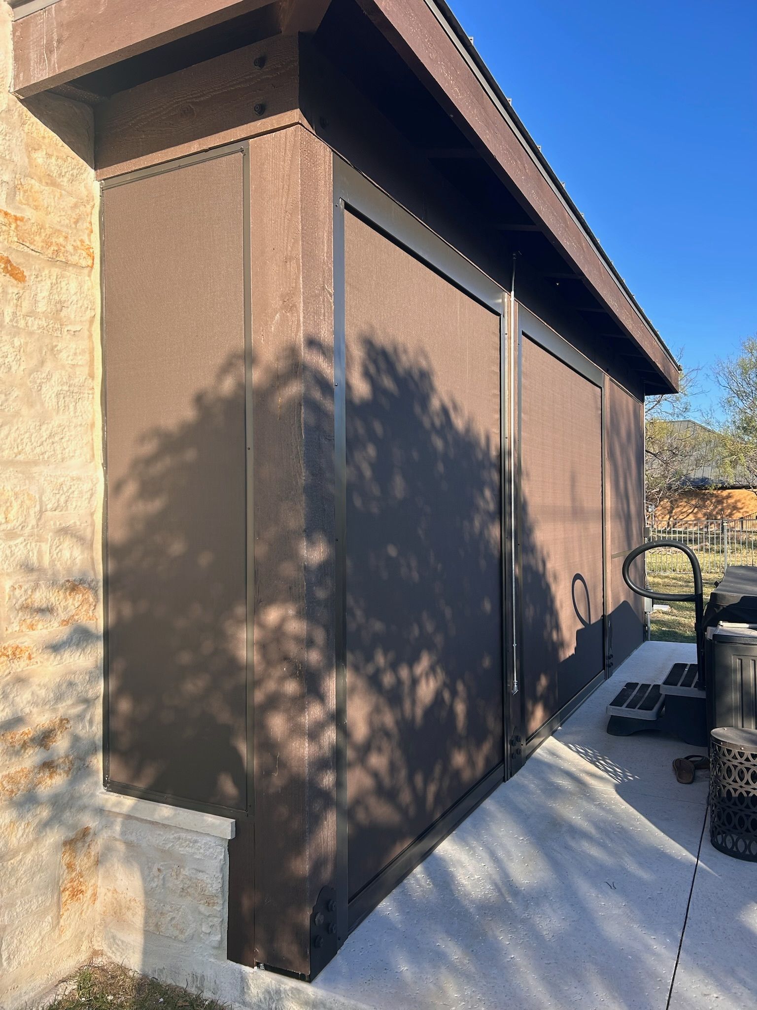 Brown storage structure attached to a building, with a dark roof and black metal trim.