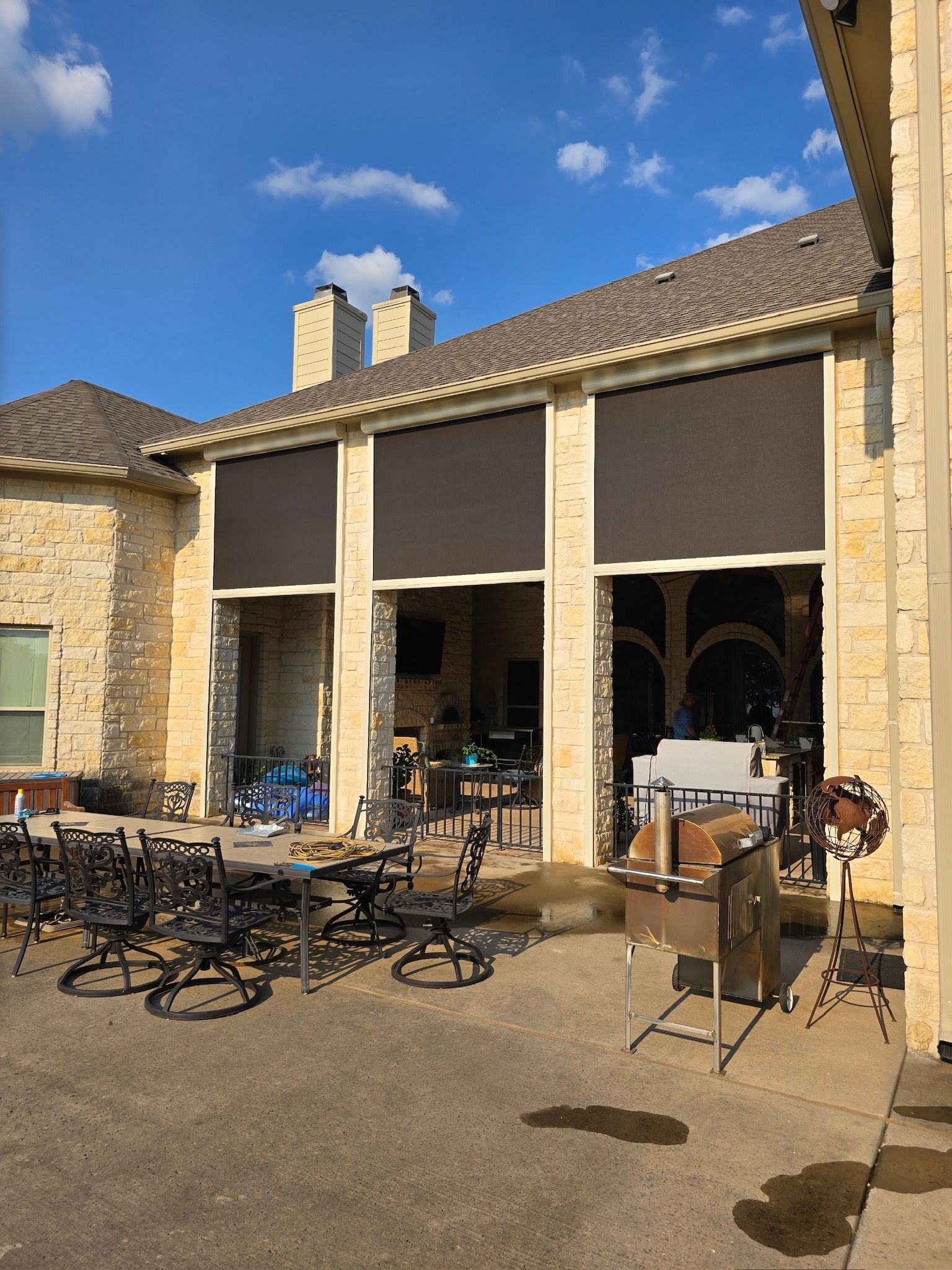 Patio with large dark retractable shades. Tables and chairs are in front of an open doorway.