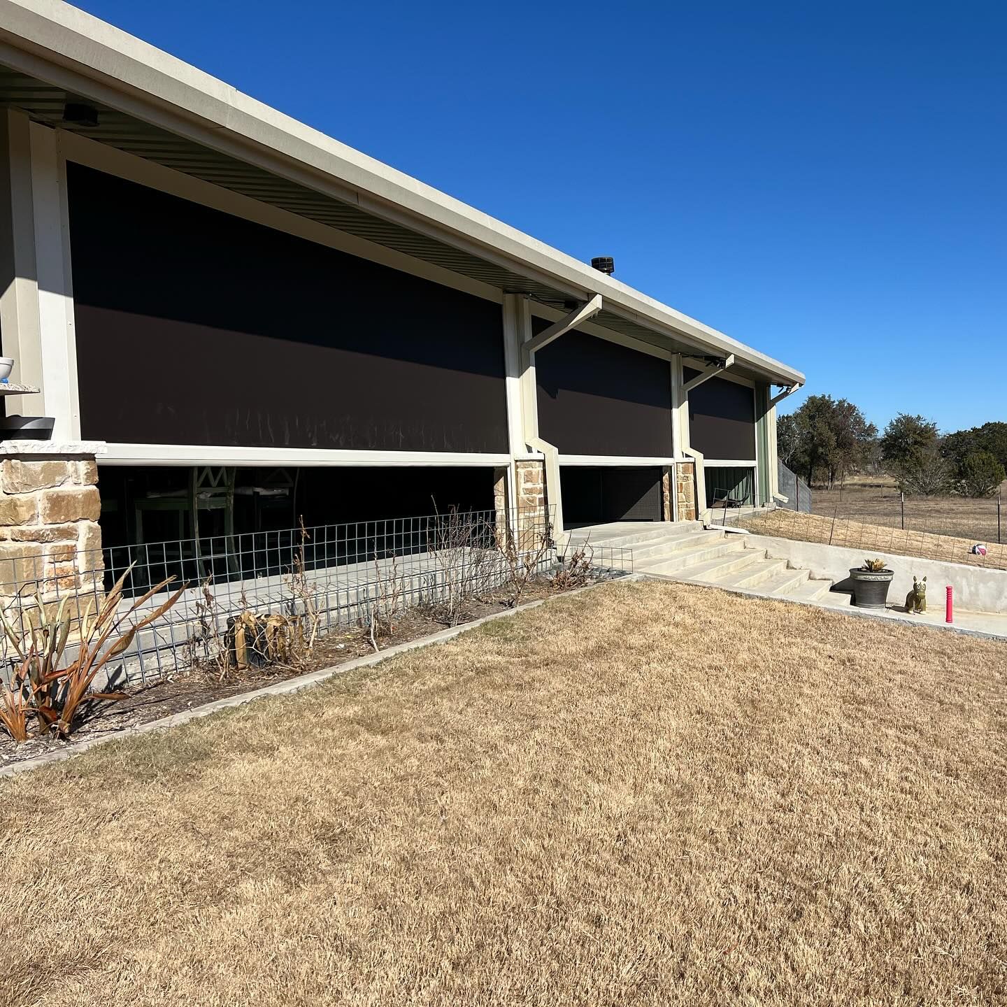 Exterior view of a building with brown shade screens over windows. A lawn is in the foreground.