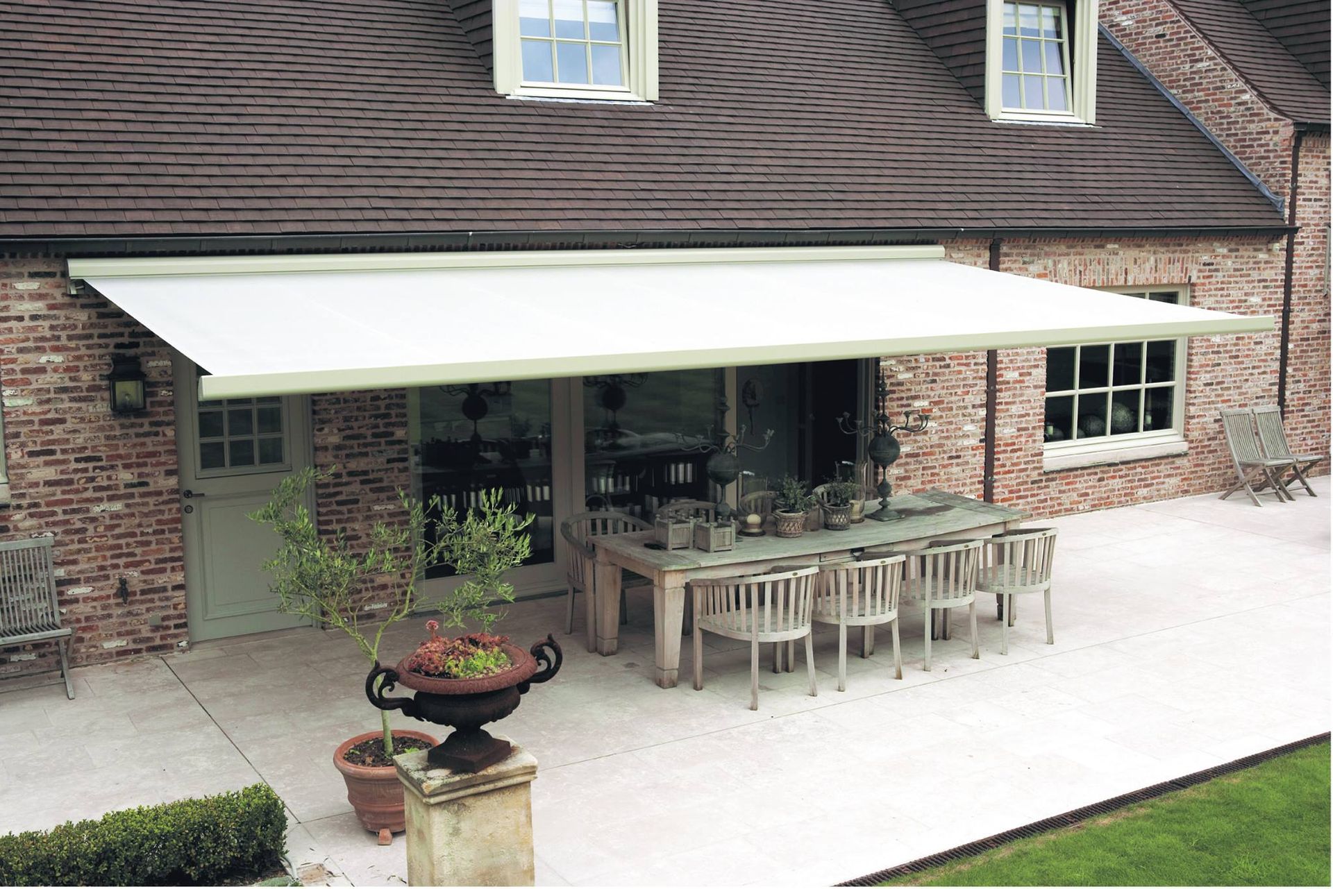 White awning shading a patio with a dining table and chairs. A brick house is in the background.