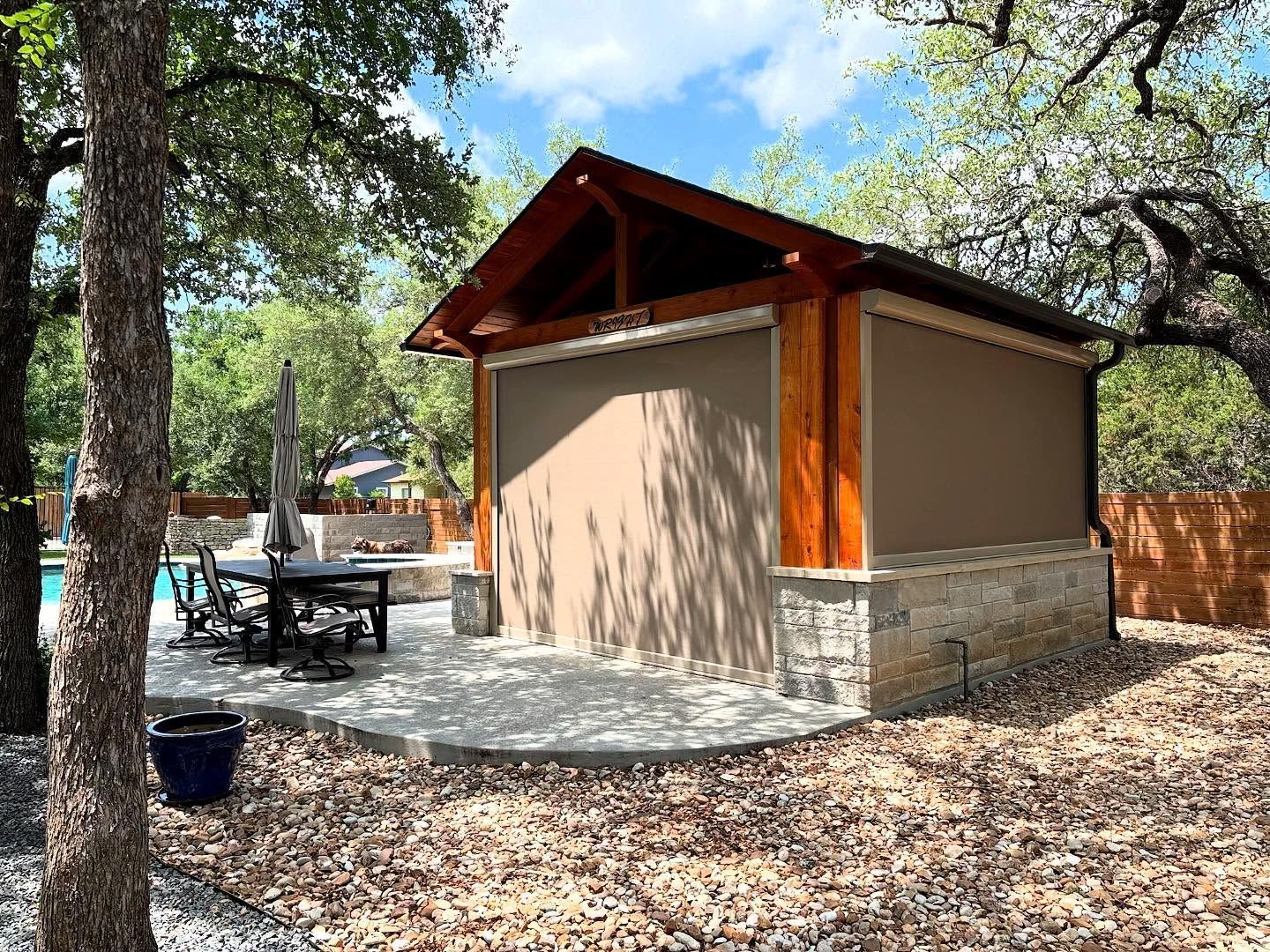 Outdoor structure with stone base and wood trim, featuring retractable shade, next to a pool.