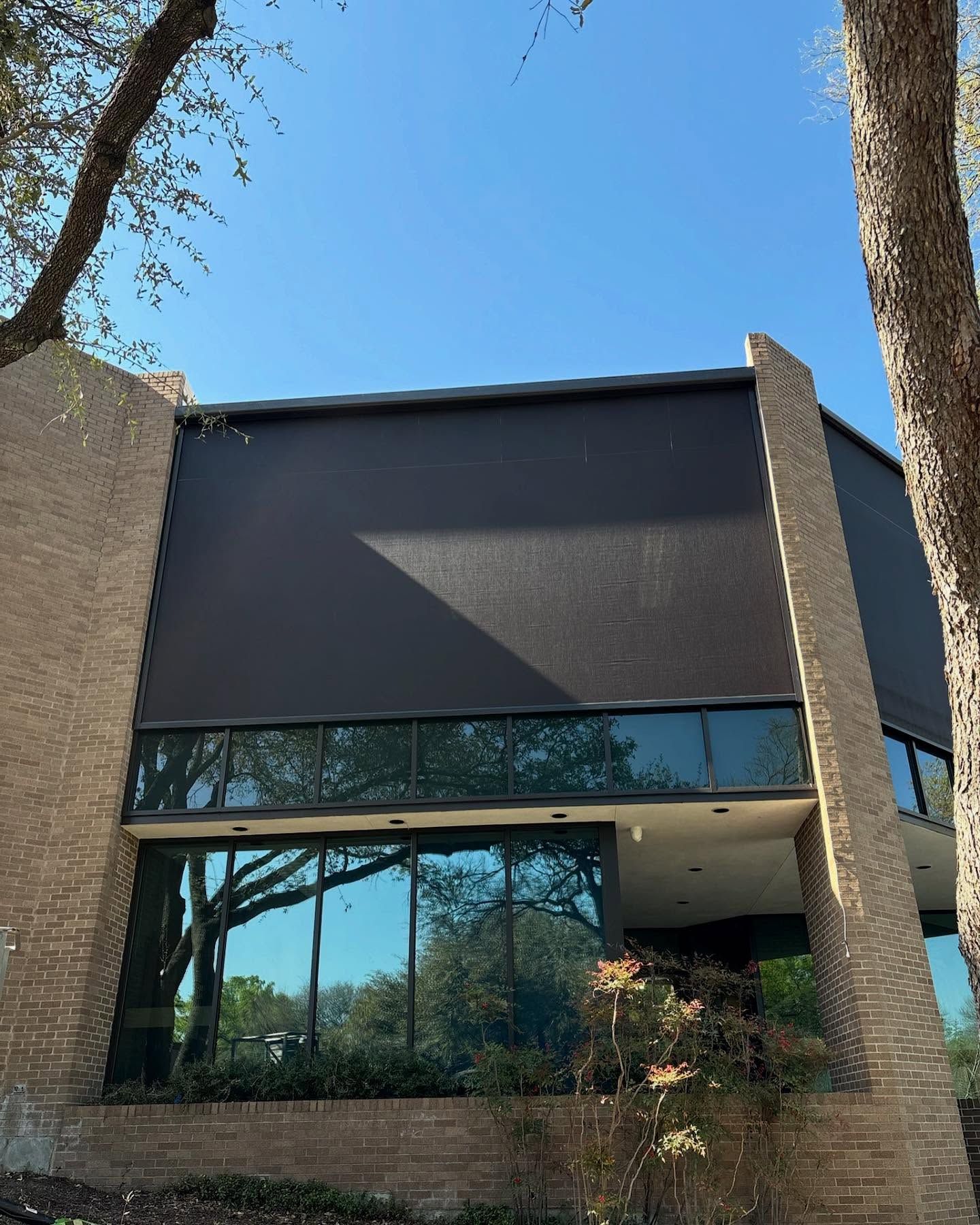 Building with dark awning and brick sides, windows reflecting trees, under a blue sky.