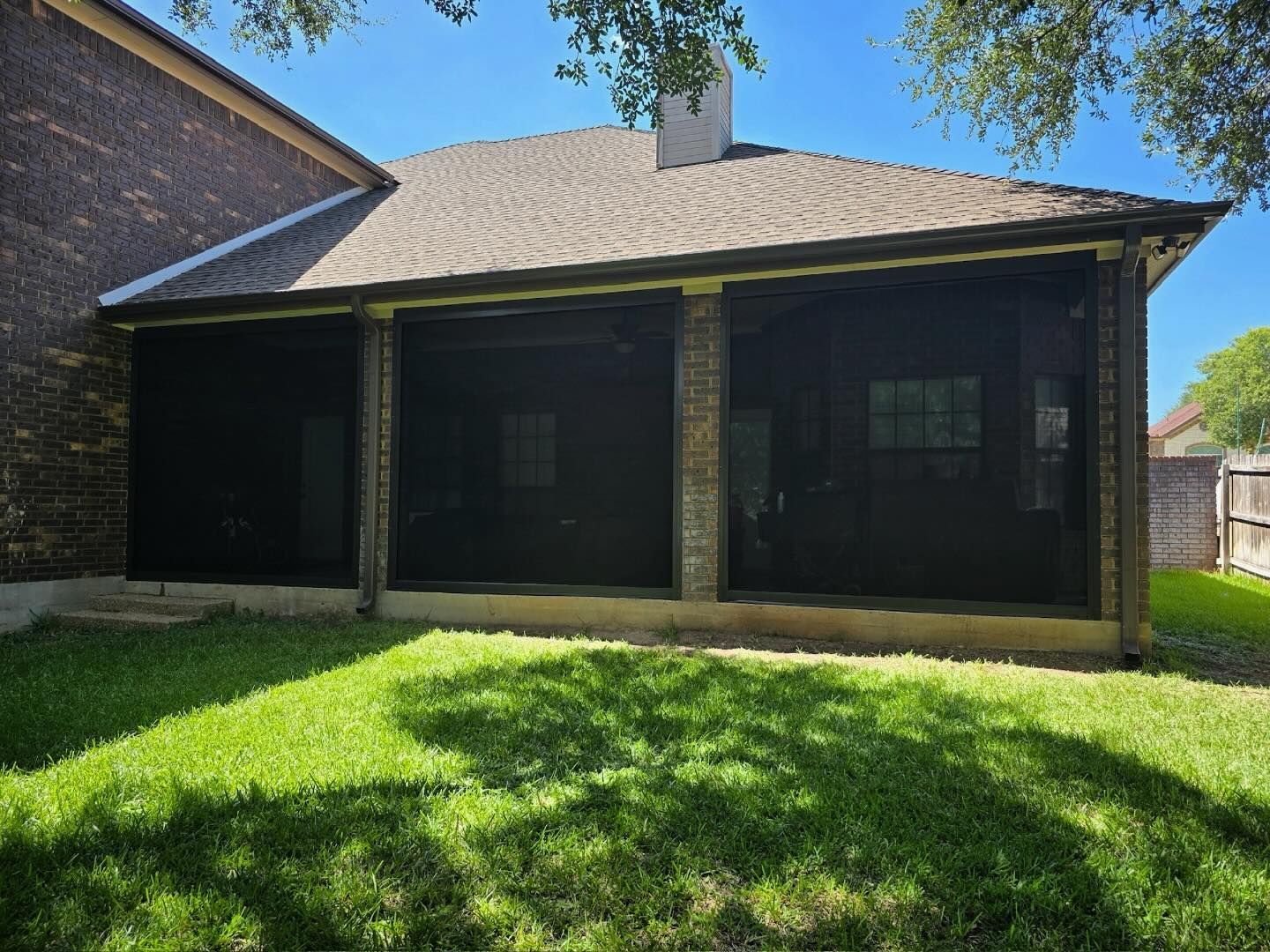 Screened-in porch on a house with brick columns. Black screens enclose the porch. Green grass and blue sky.