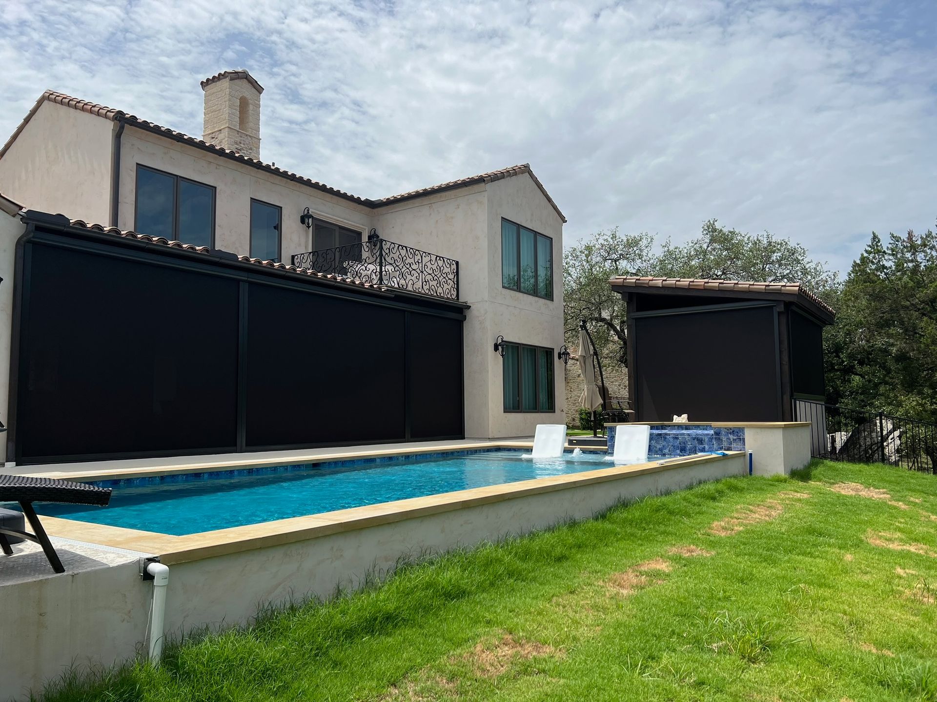 Exterior view of a house with a swimming pool and black sun shades, set against a cloudy sky.