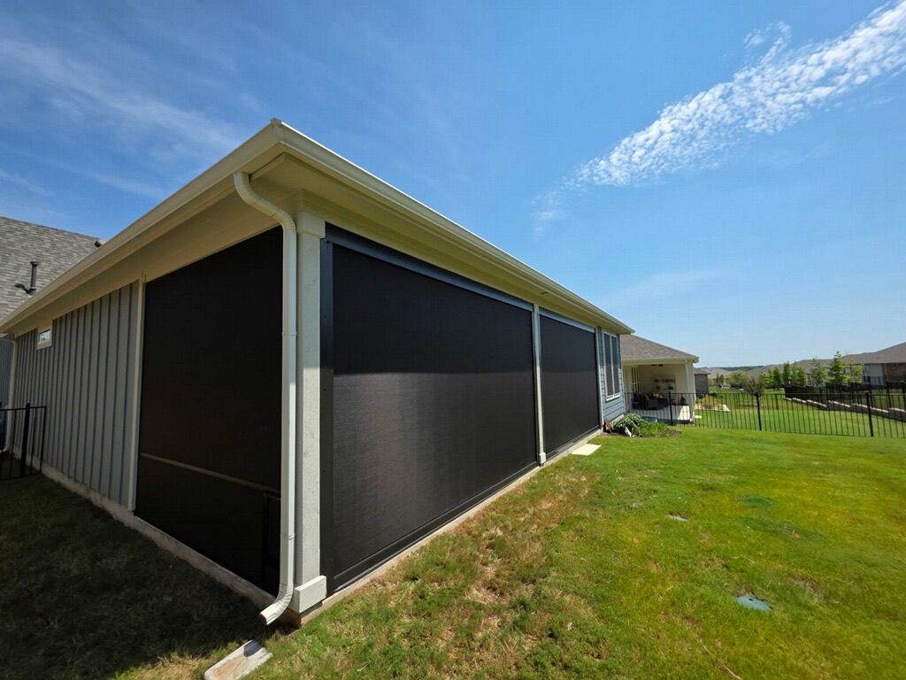 Black retractable screens on a house exterior, green lawn, blue sky.