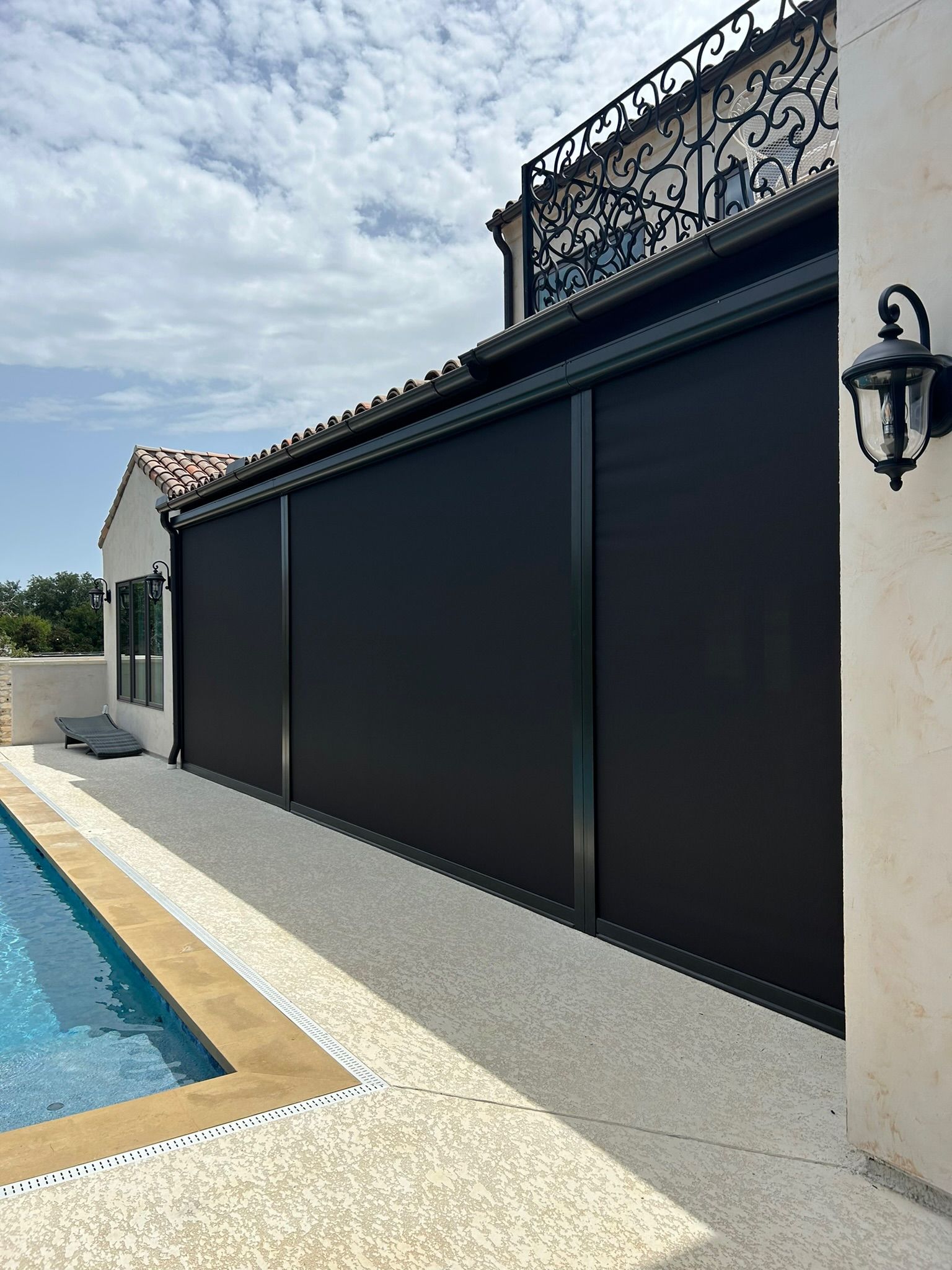 Black retractable shades along an outdoor patio wall next to a swimming pool.