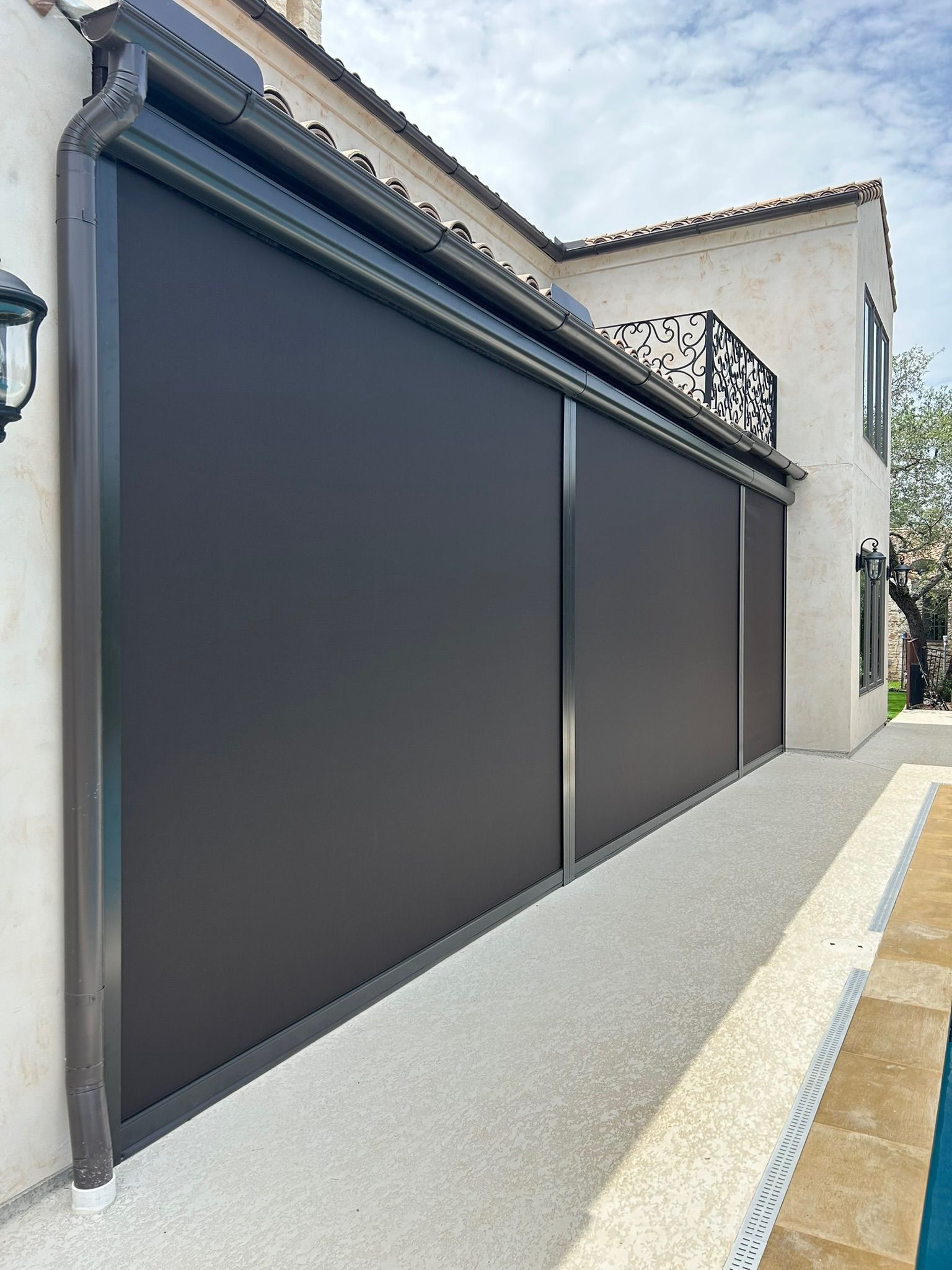 Exterior view of a home with dark-colored retractable shades installed on the side, near a swimming pool.