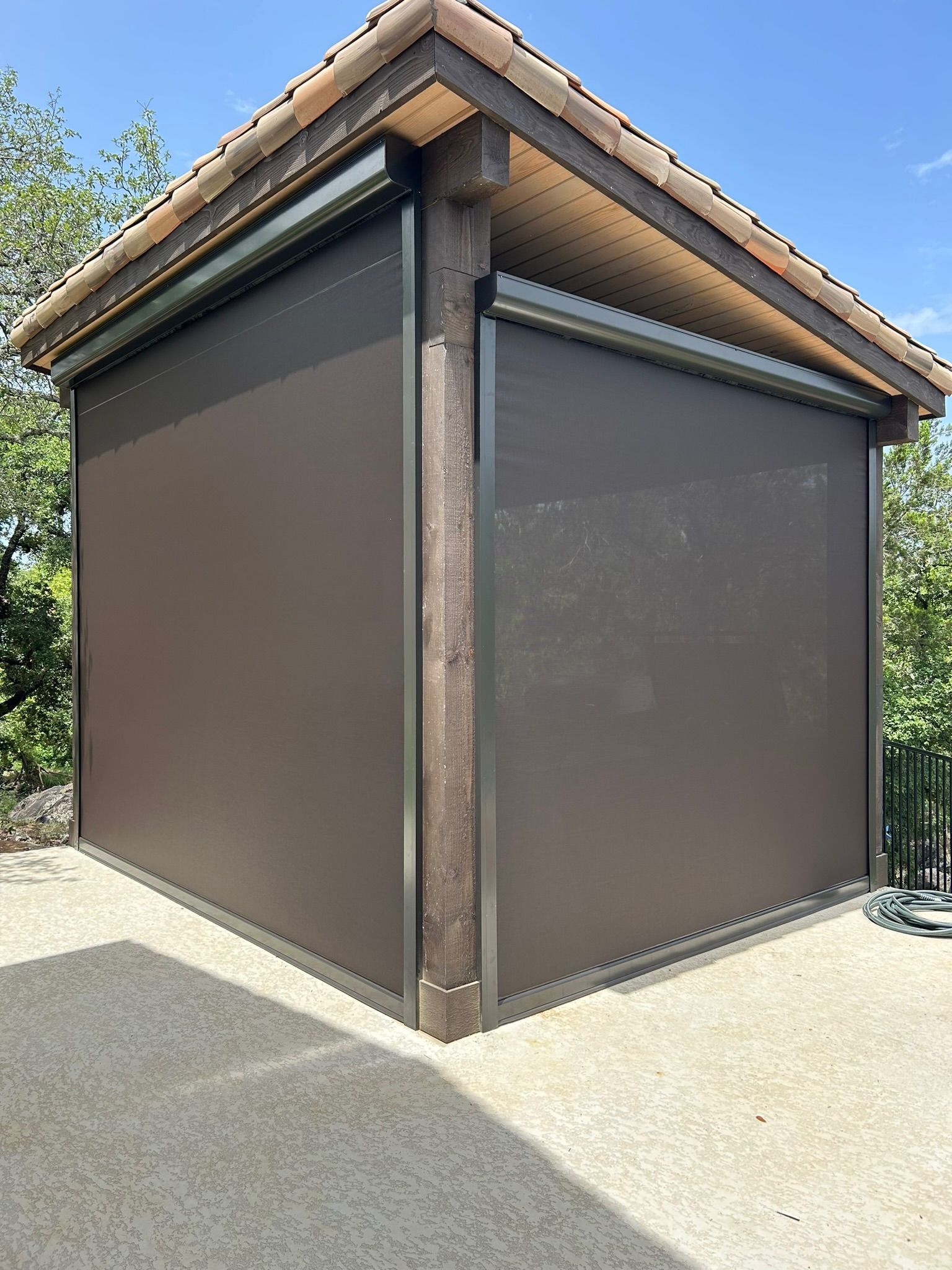 Brown outdoor shades on a covered structure, likely a patio or gazebo, under a tiled roof.