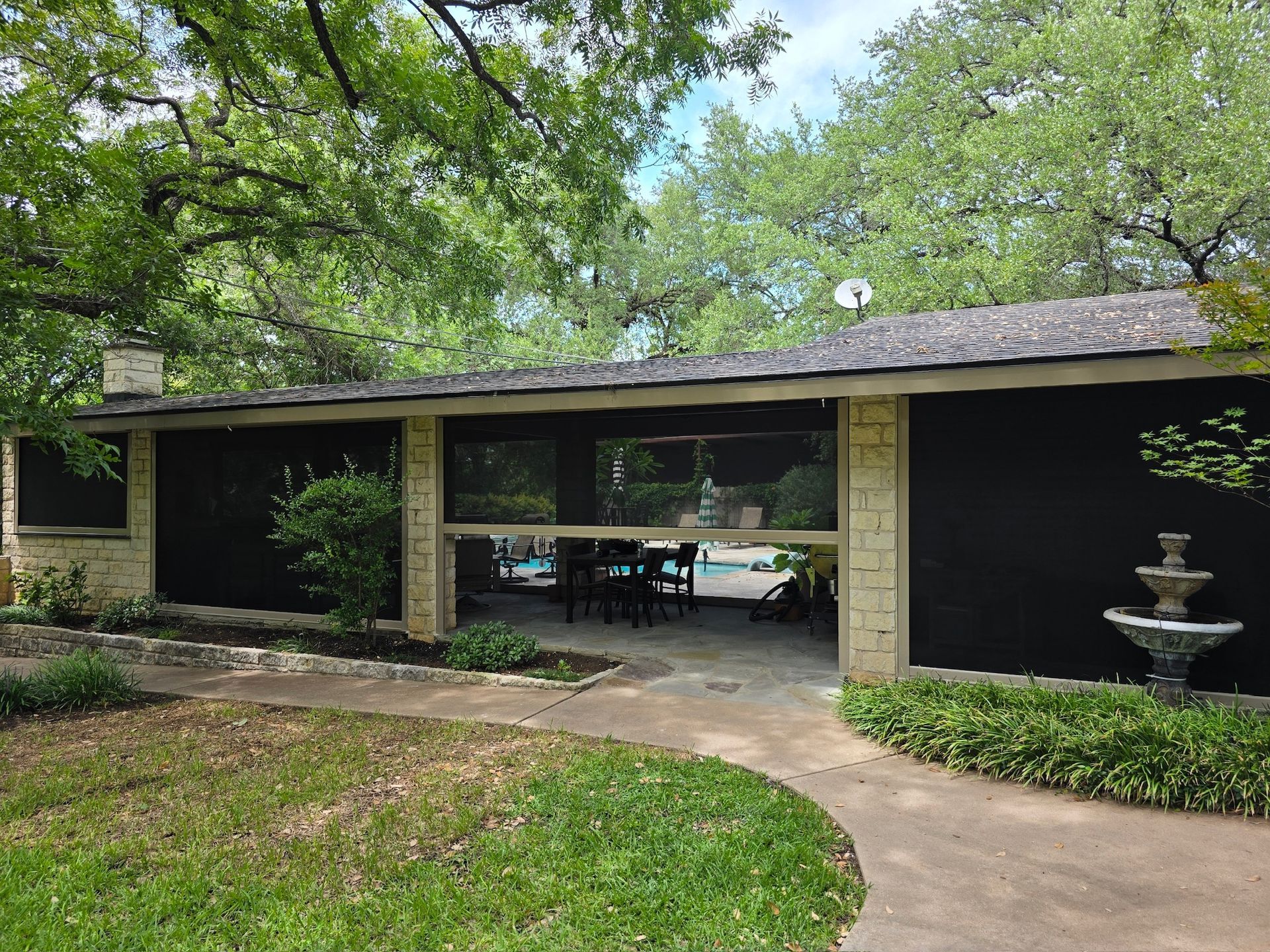 Outdoor pavilion with black screens, stone pillars, a fountain, and trees.