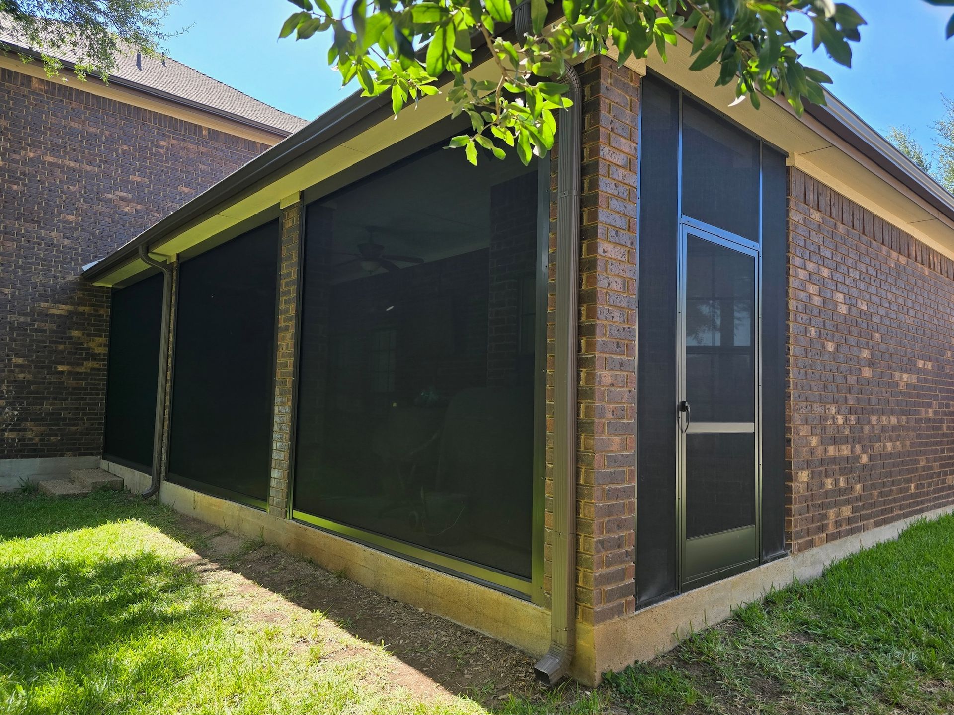 Screened-in porch attached to a brick house, featuring dark screens and a door.