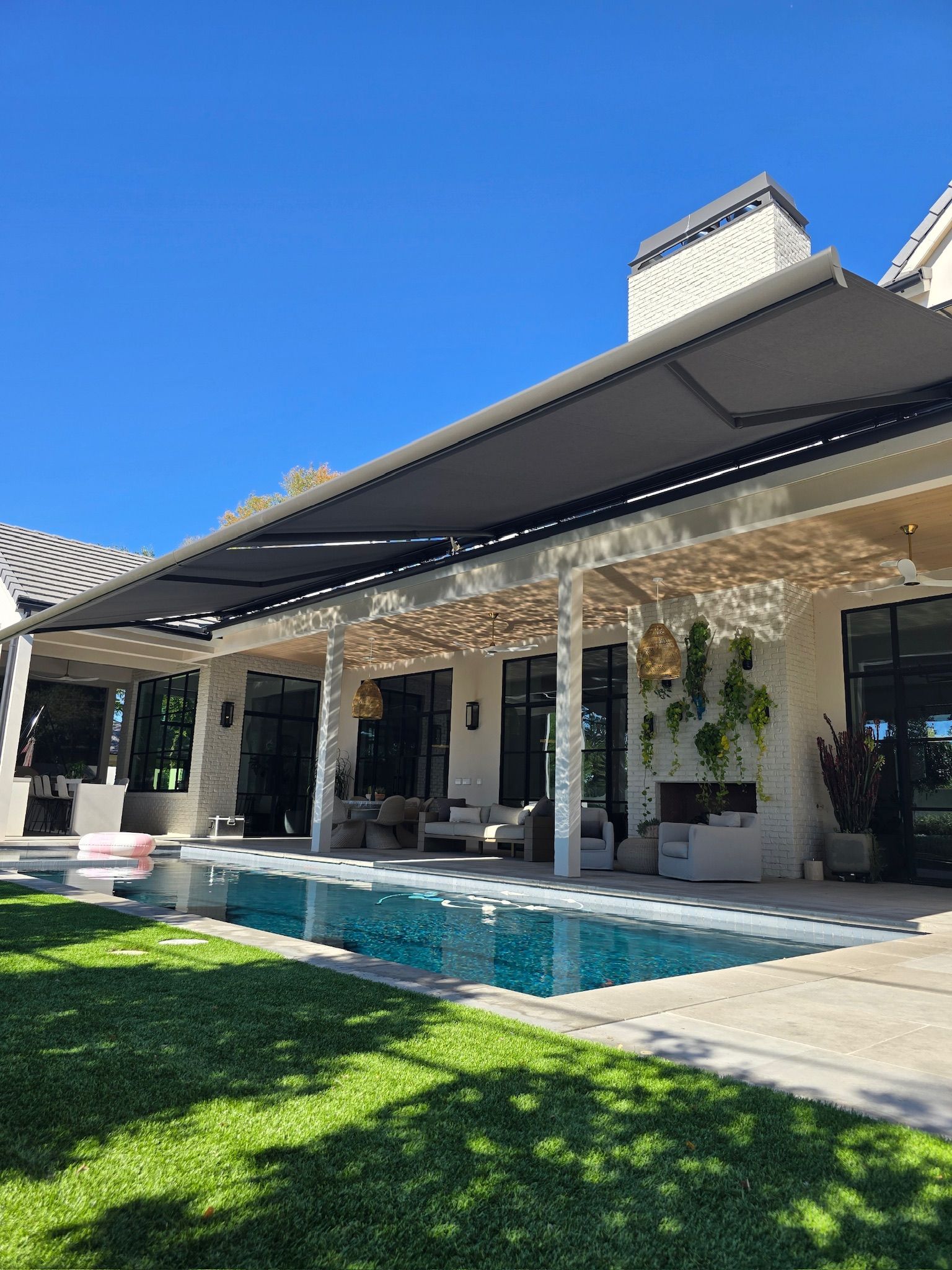Modern home with retractable awnings over a patio, pool, and green lawn on a sunny day.