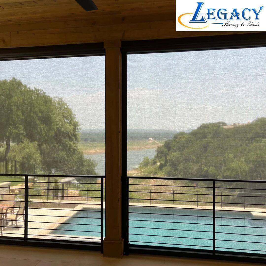 Poolside view through a window with sun shades, overlooking a lake and hills.