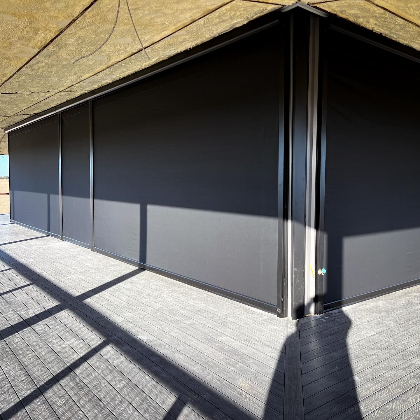 Dark gray building exterior with sunlit wooden deck and shadows.