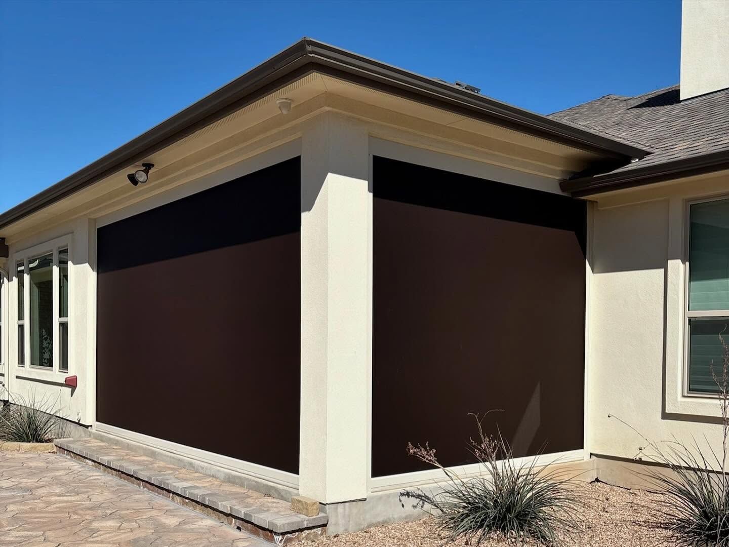 Brown outdoor shades on a cream-colored patio, next to a house with beige walls.