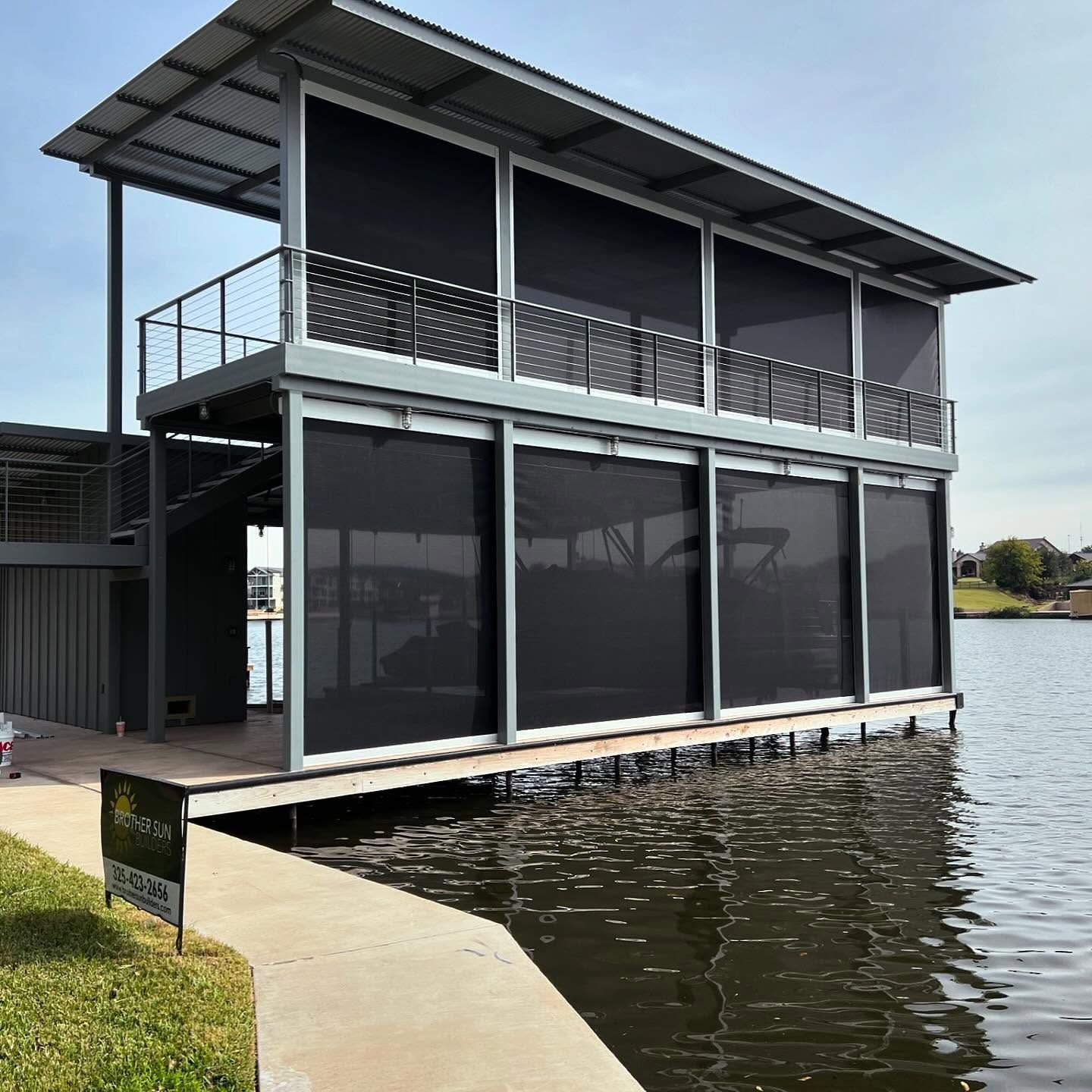 Two-story lakeside building with black roller shades. Metal roof and railing. Located on a dock.