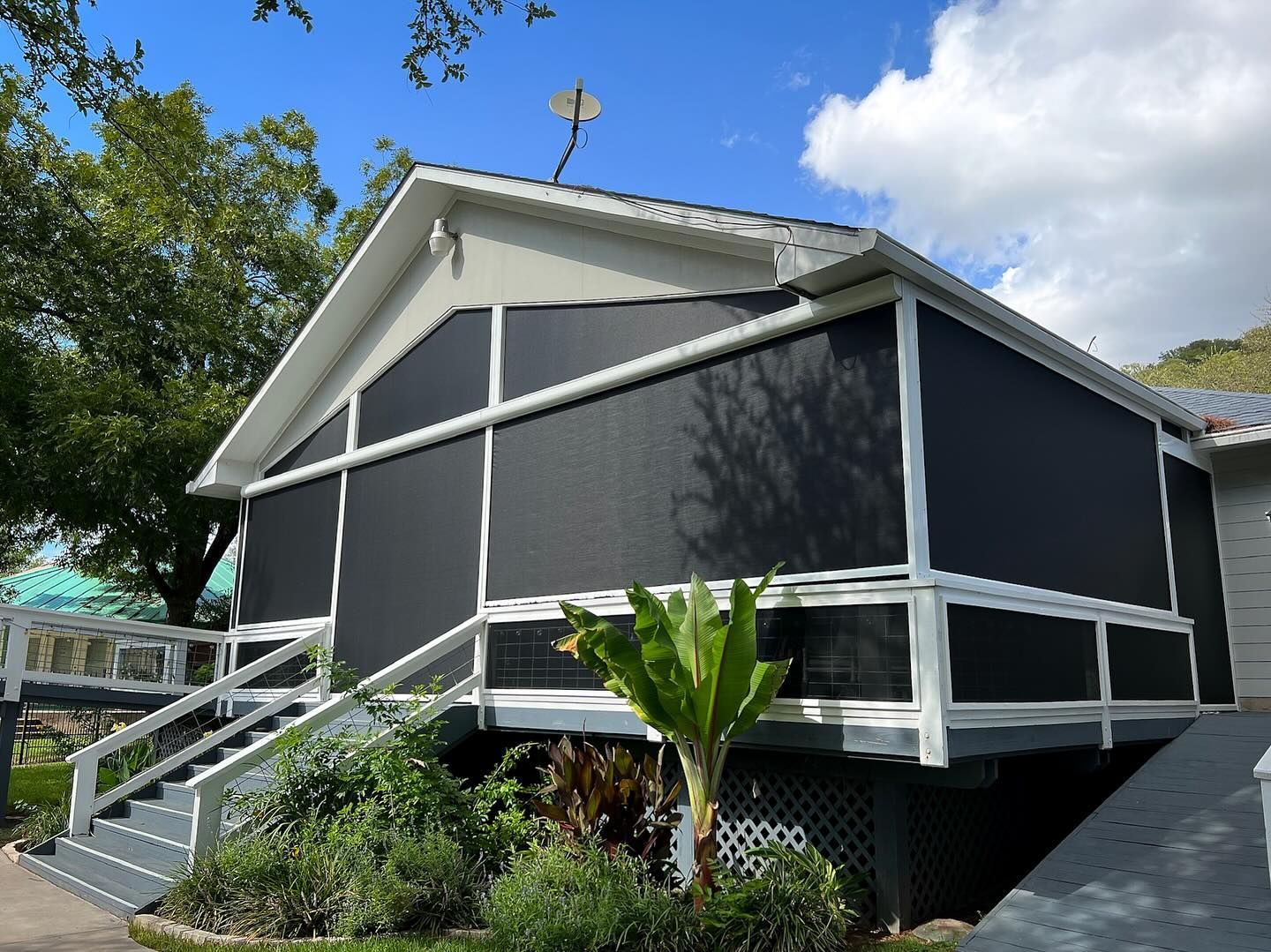 A house with gray siding, white trim, and black screens on the porch.  Exterior stairs lead to the porch.  Sunny day.