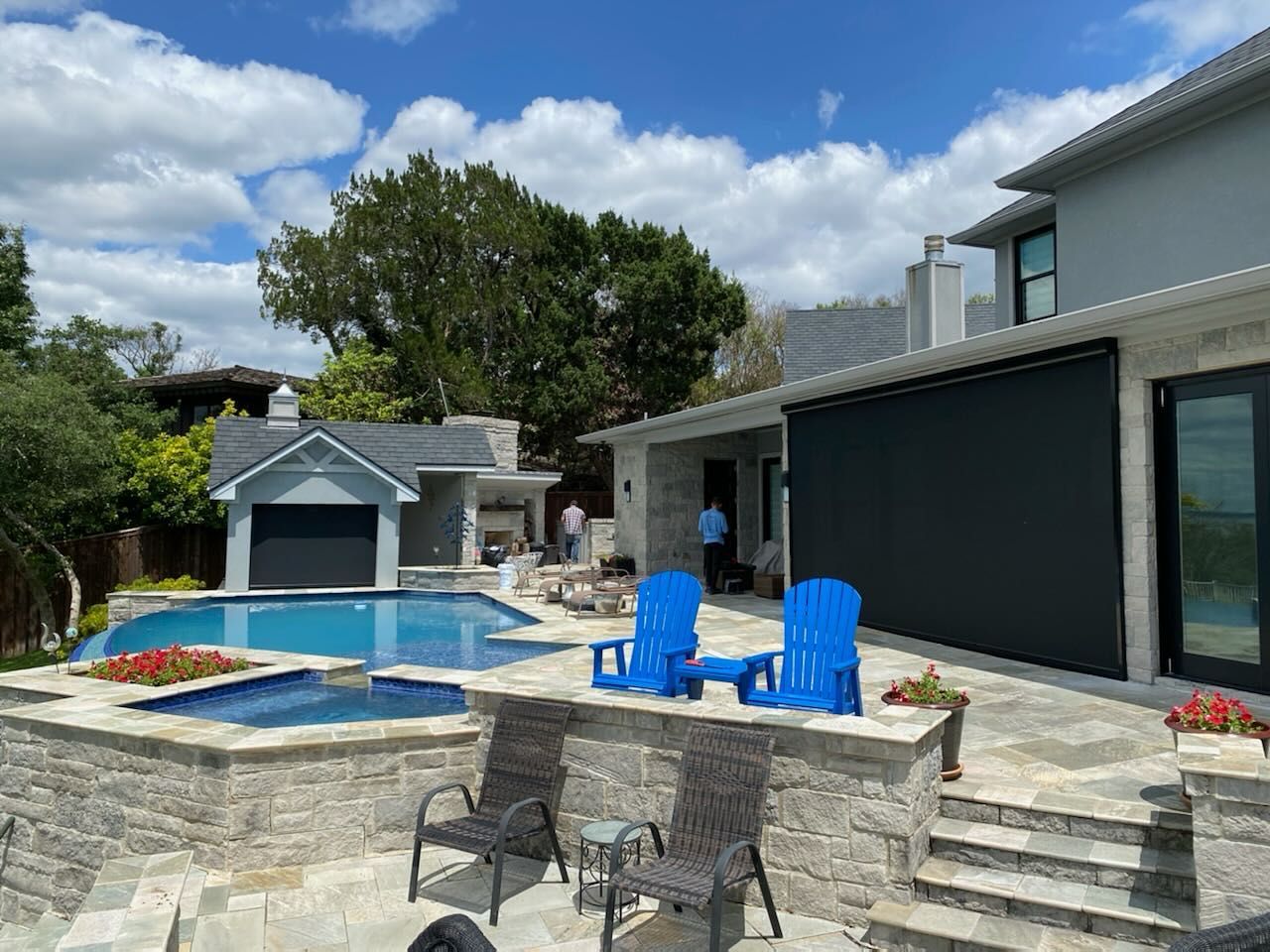 Backyard with pool, patio, and modern house; blue chairs and a black roll-down shade.