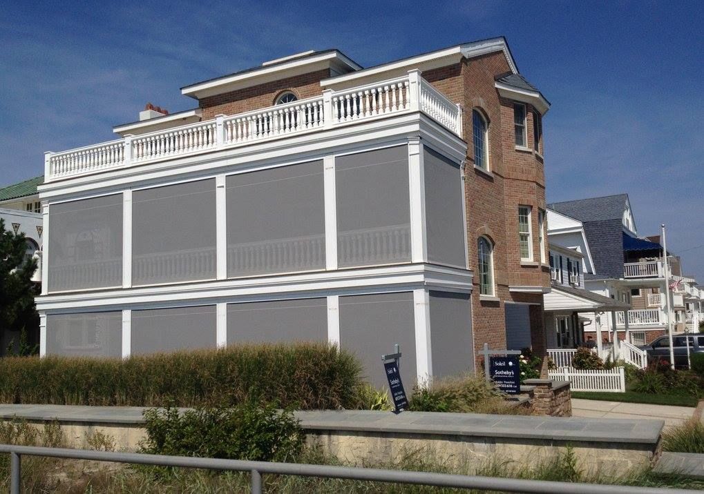 A multi-story brick building with grey sun screens. White railings and trim. Sunny day.