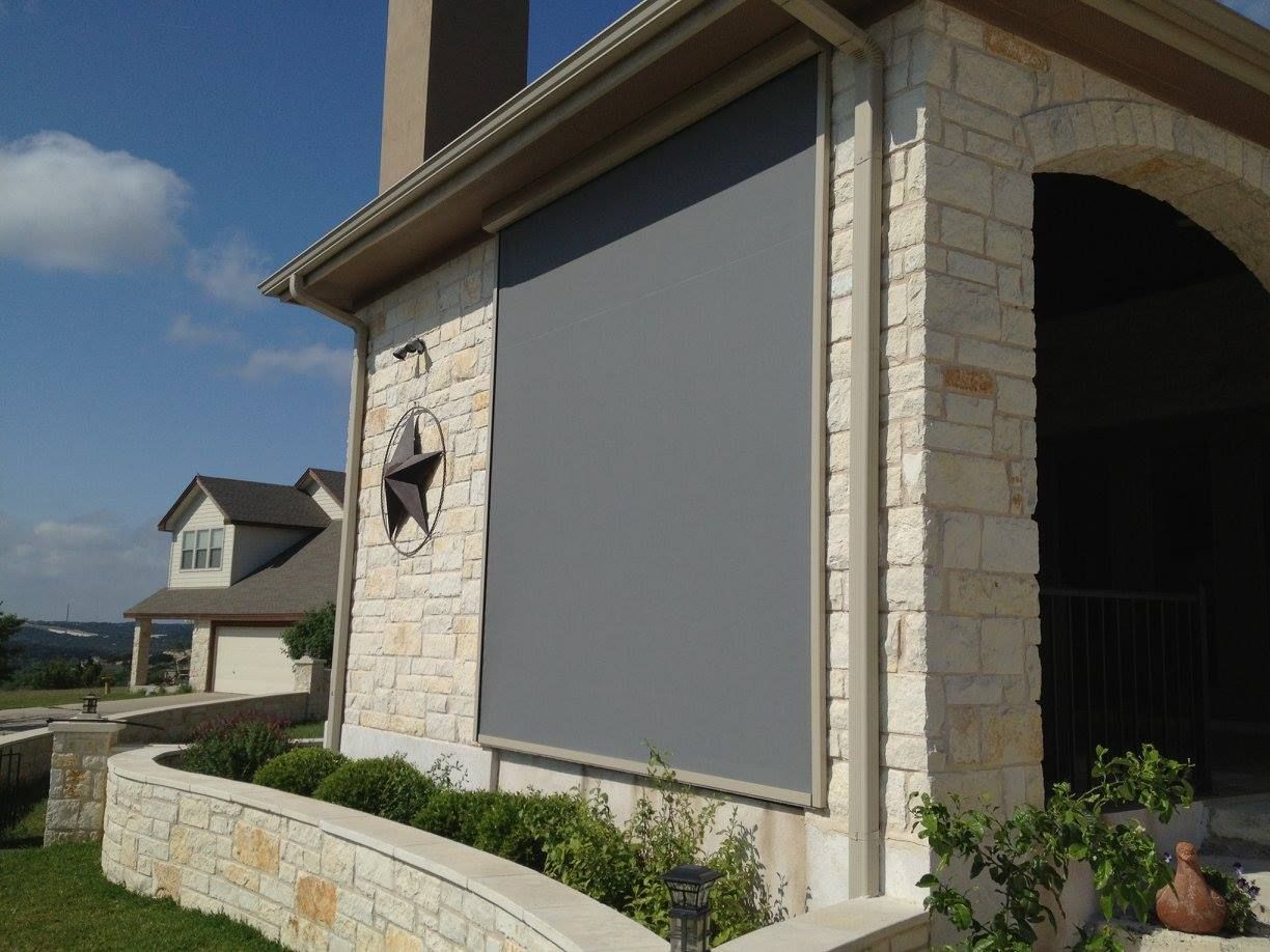Exterior of a house with a large gray sun shade extended, on a sunny day.