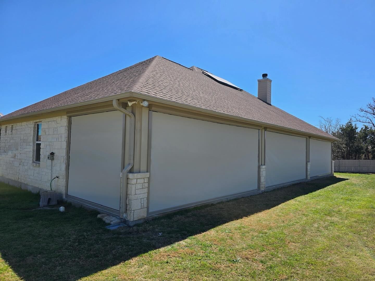 Exterior of a house with beige screens covering windows, under a brown roof, on a sunny day.